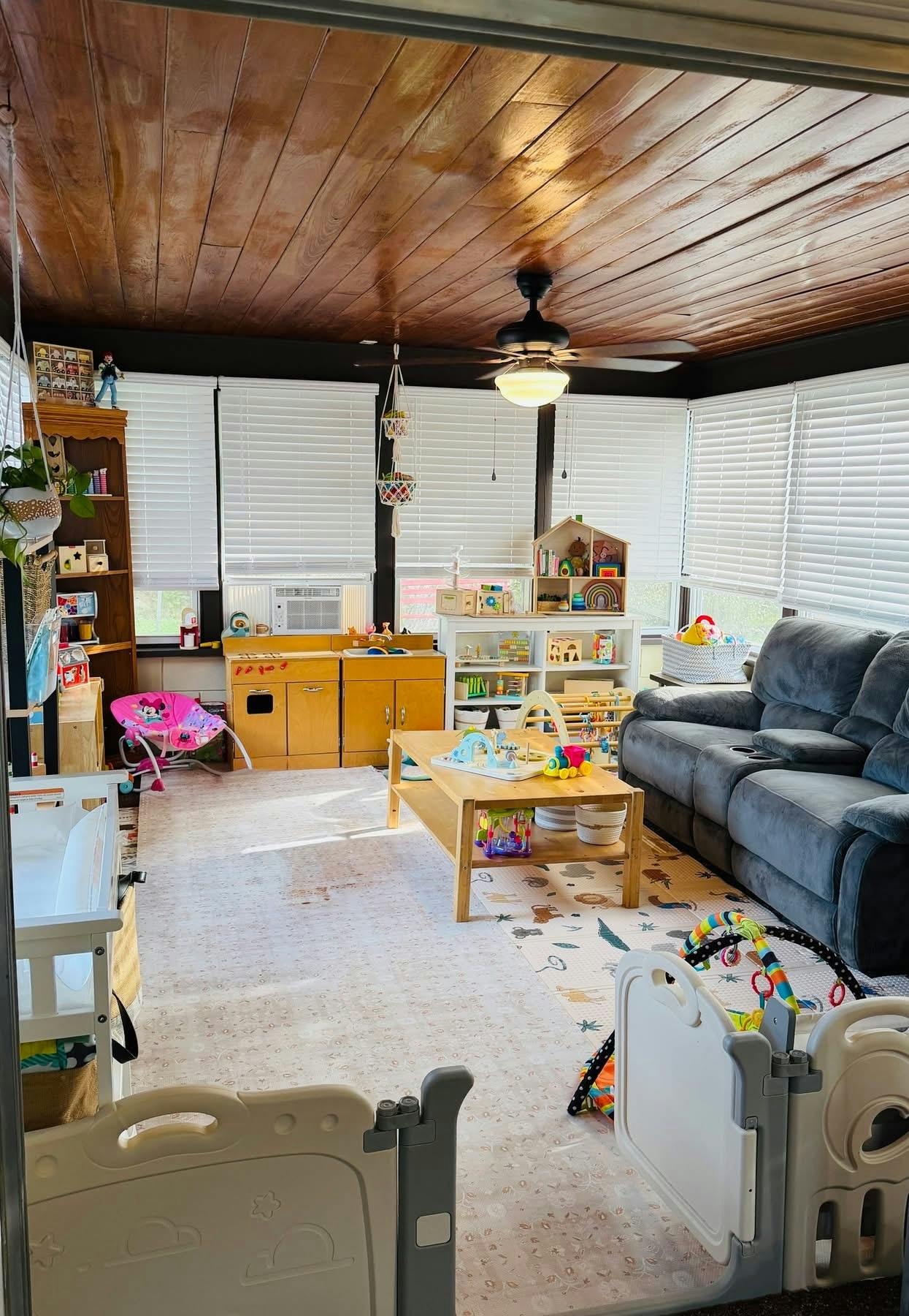 A playroom filled with toys, a small wooden kitchen, and a grey sofa