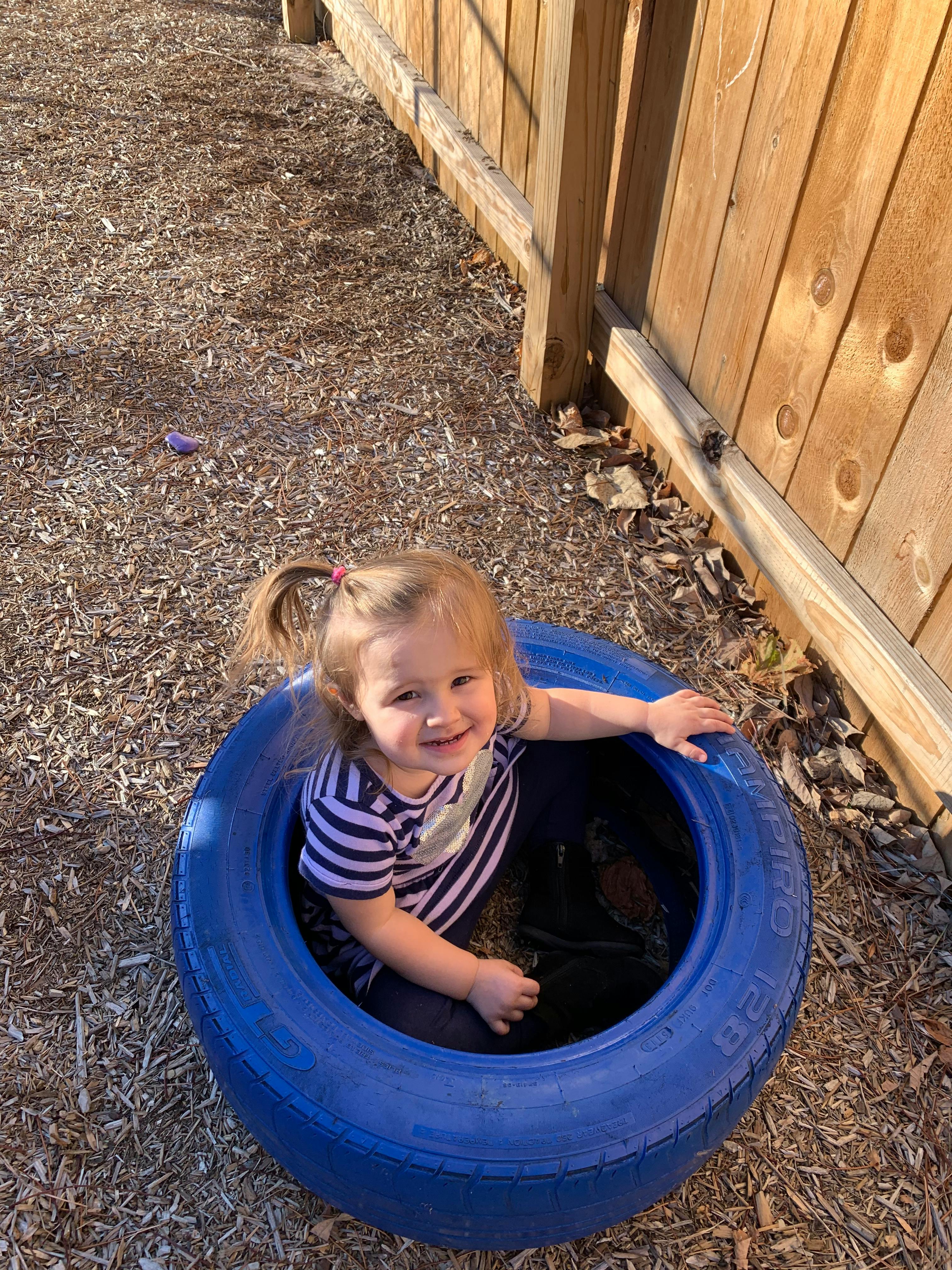 Child sitting in a blue tire on wood chips