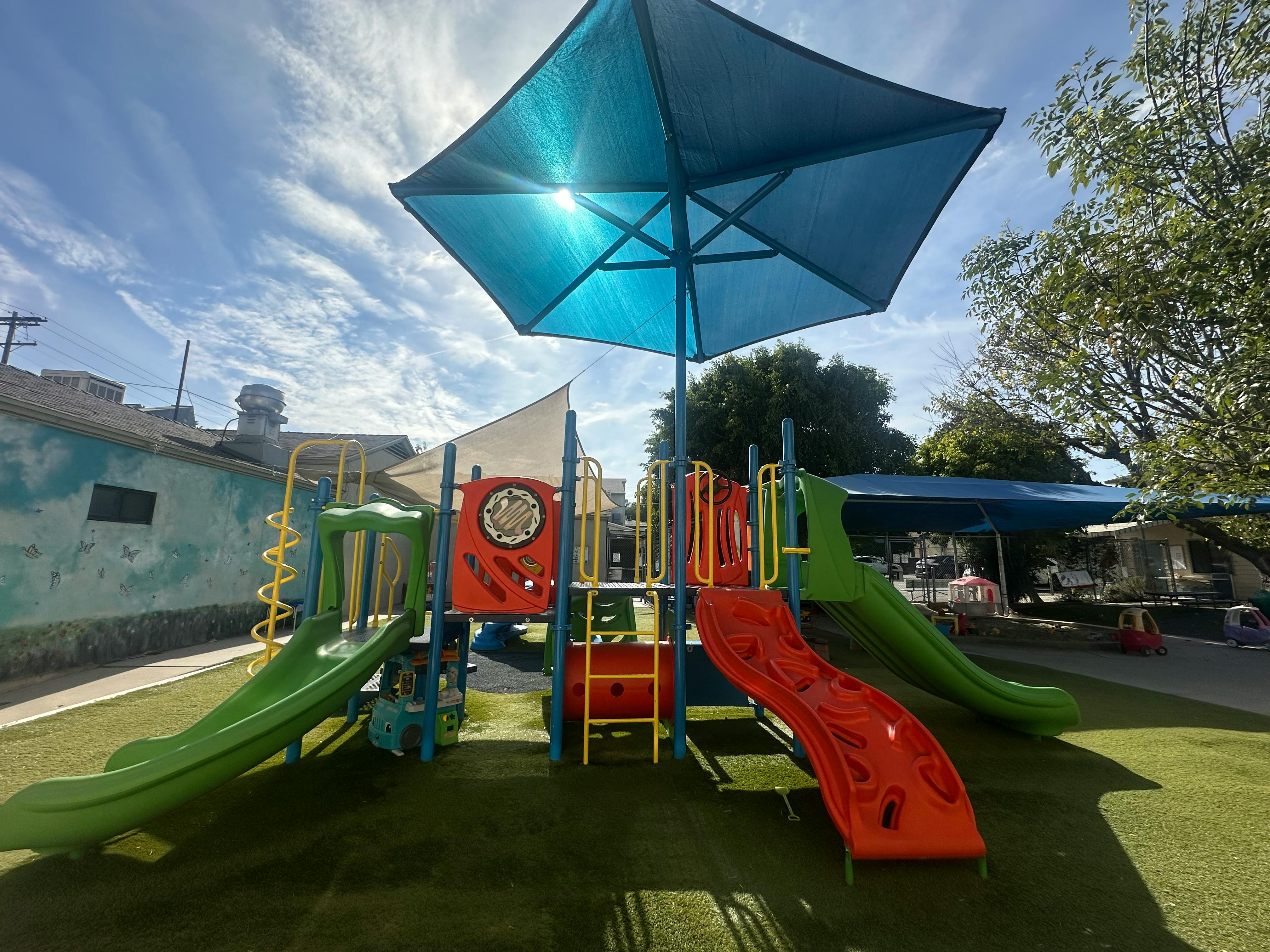Playground with slides and climbing structures under a large blue umbrella