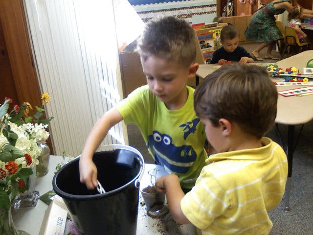 Two children playing with a bucket and dirt