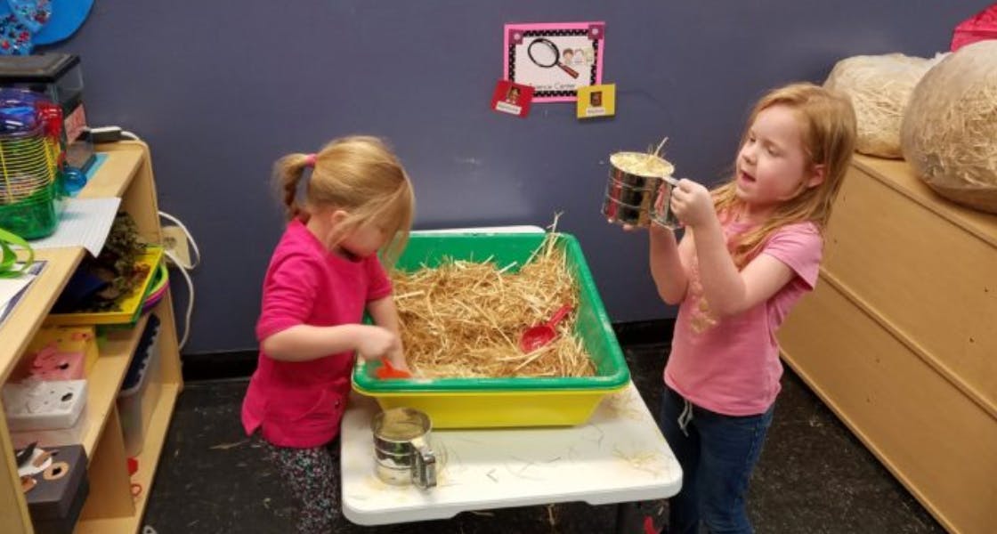 Two children playing with straw in a bin