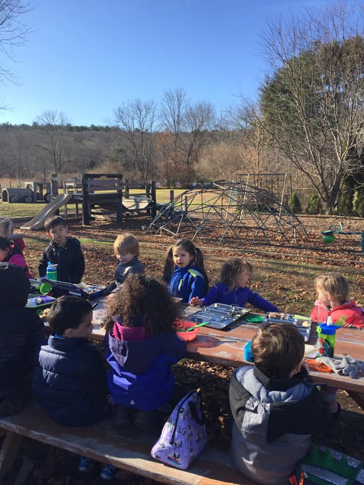 Children sitting at a picnic table outdoors with a playground in the background