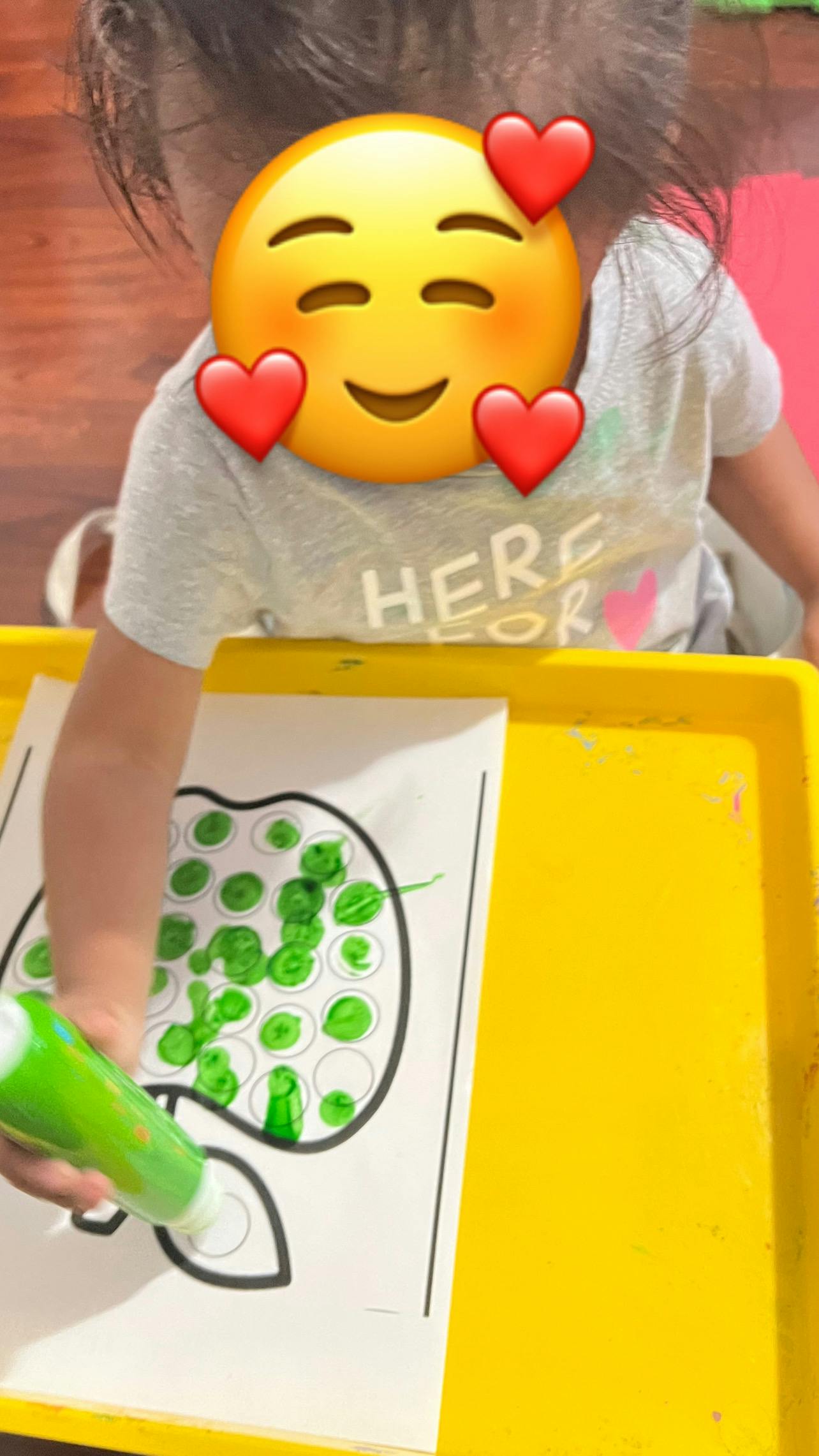 Child using a green paint marker to dot an apple worksheet