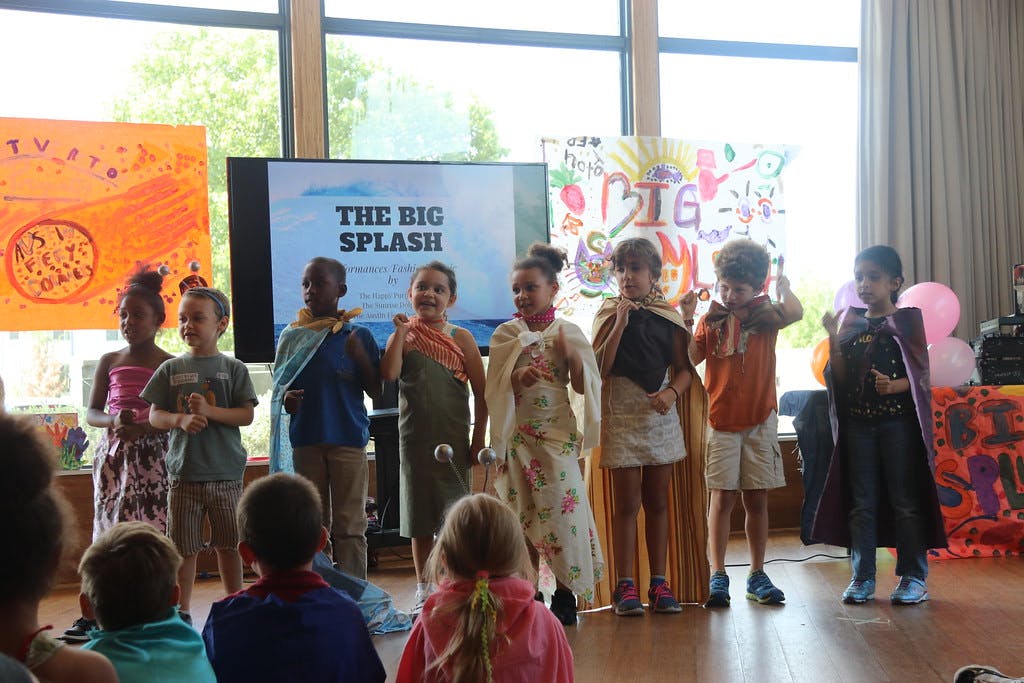 Children in costumes on a stage with a screen displaying "THE BIG SPLASH"