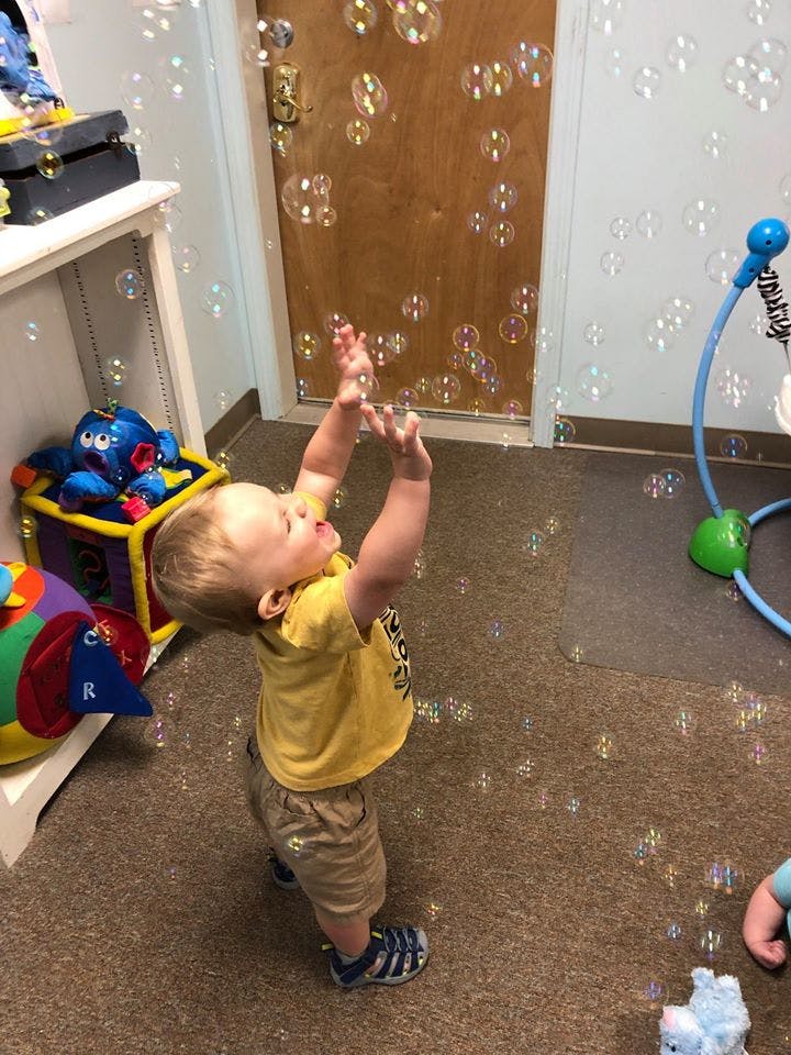 Child reaching up to catch bubbles indoors