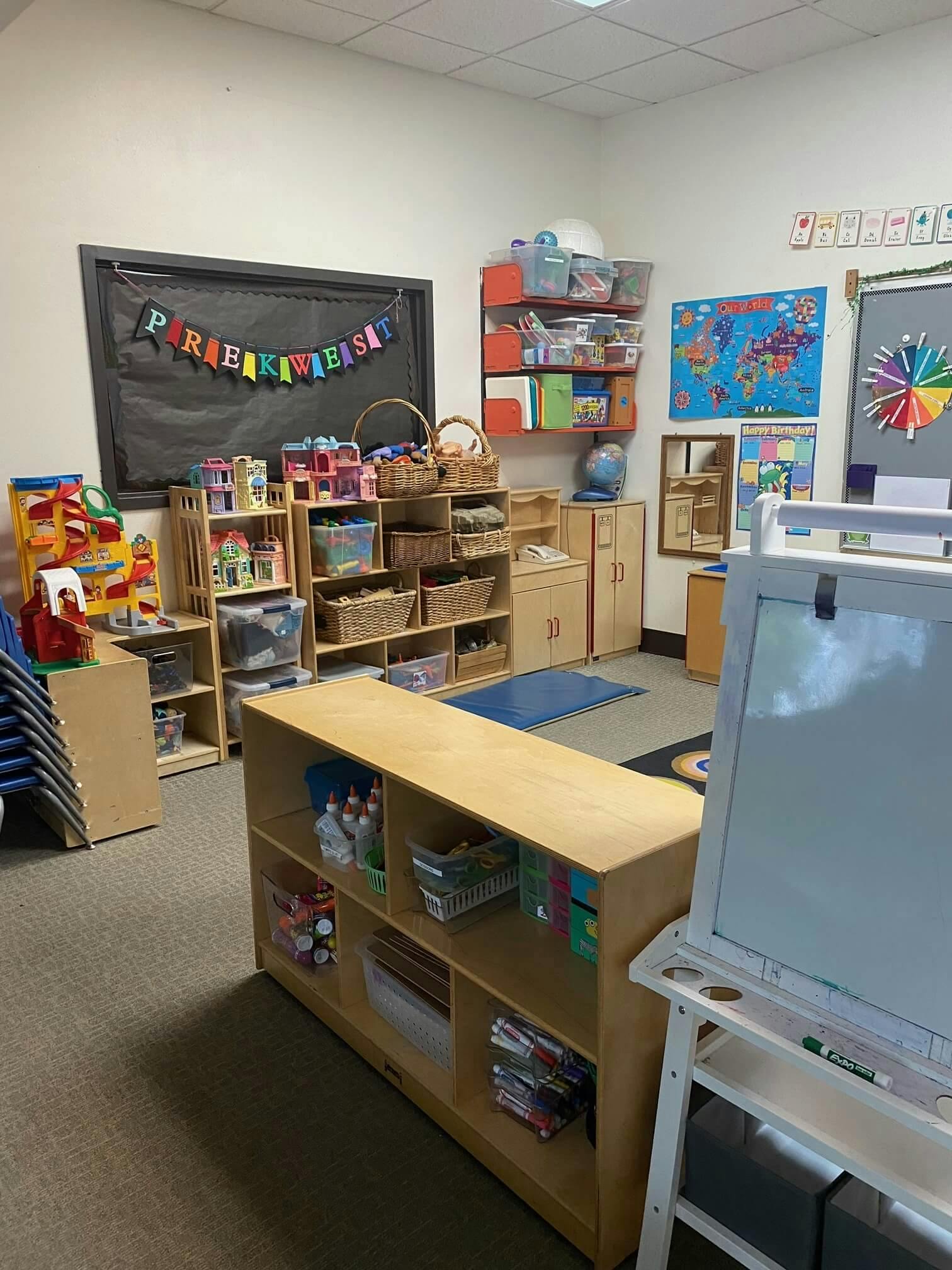 Classroom with shelves of toys, supplies, and a "PREKWEST" banner