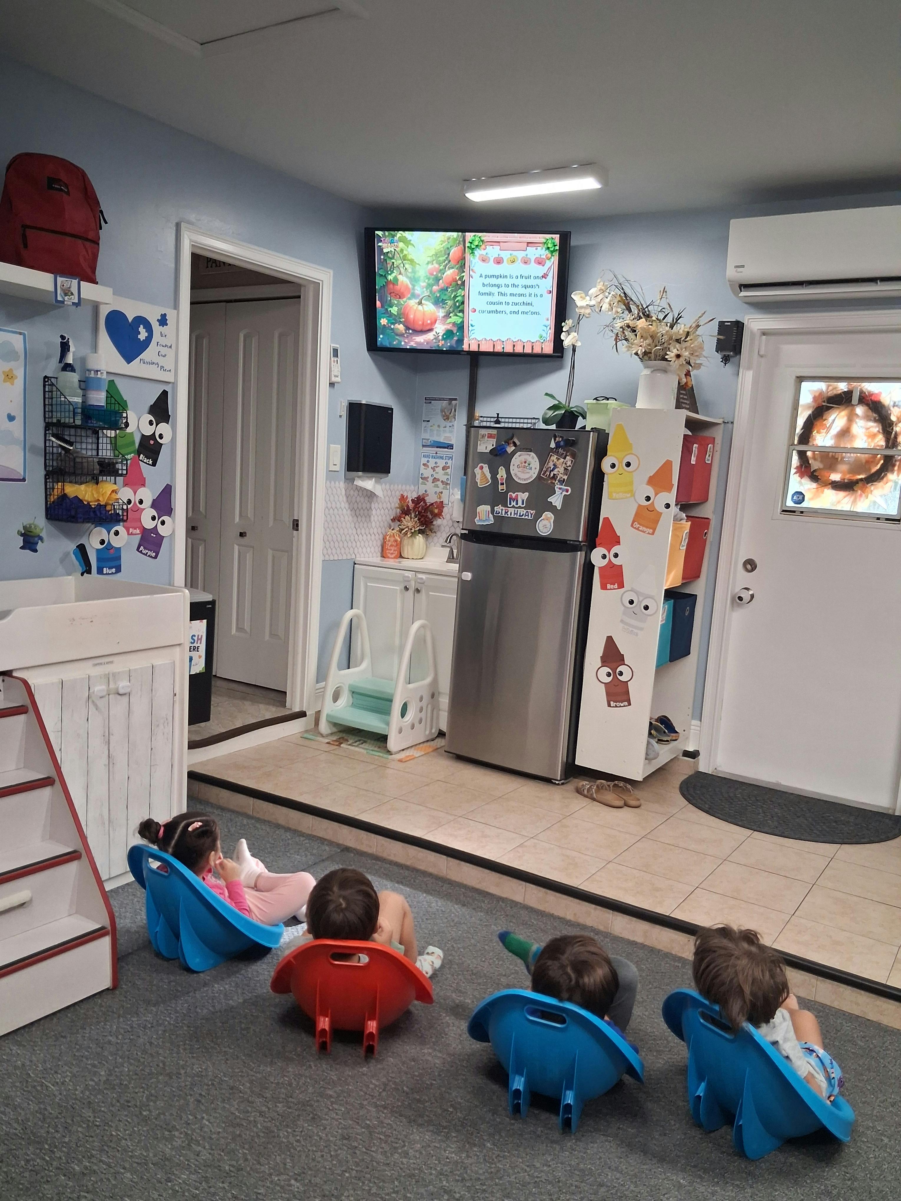 Children sitting in chairs watching a television screen in a classroom