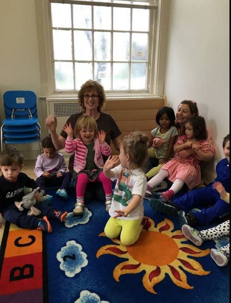 Adults and children sitting on a colorful rug in a classroom