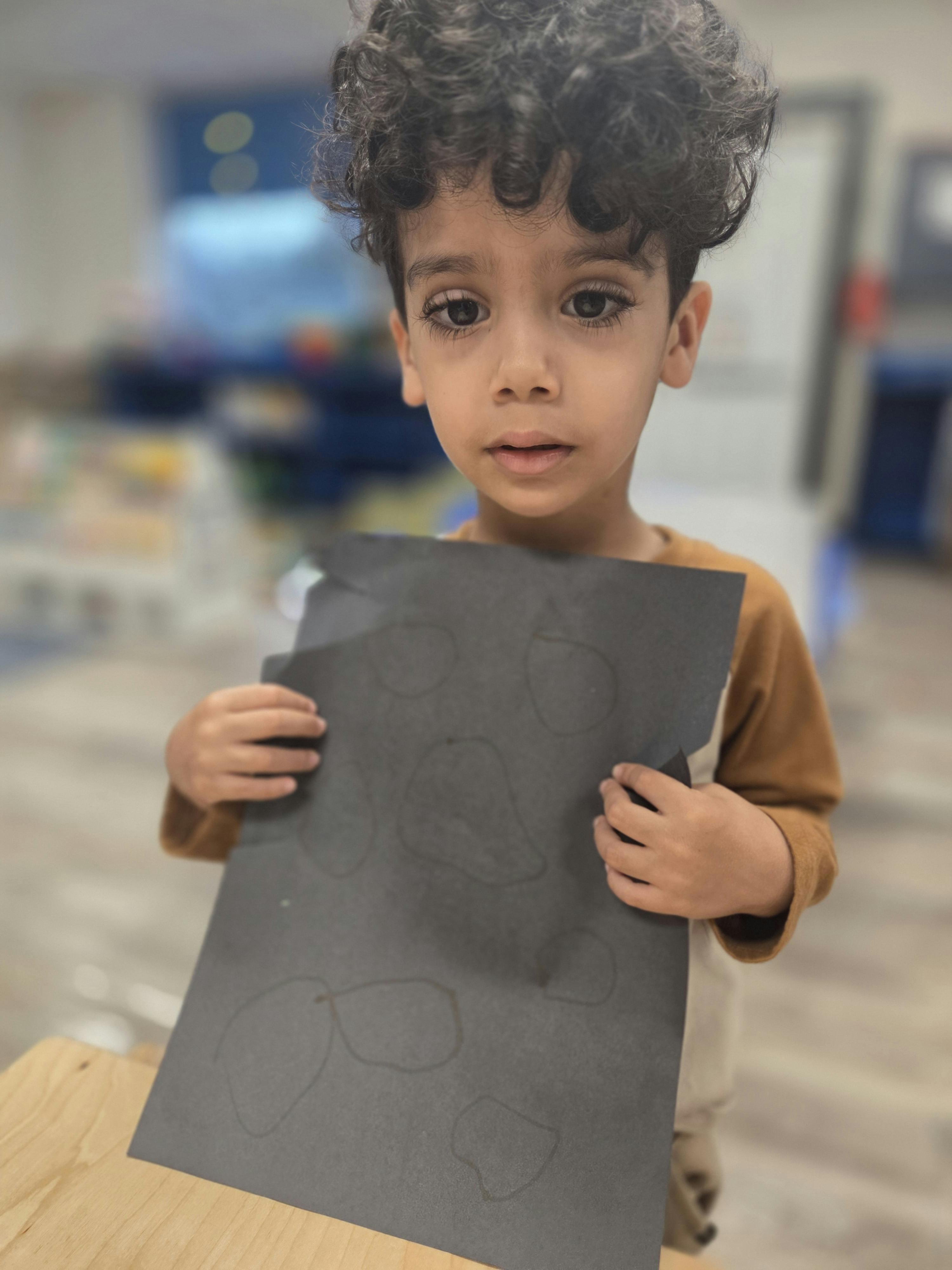 Child holding up a black piece of paper with faint drawings