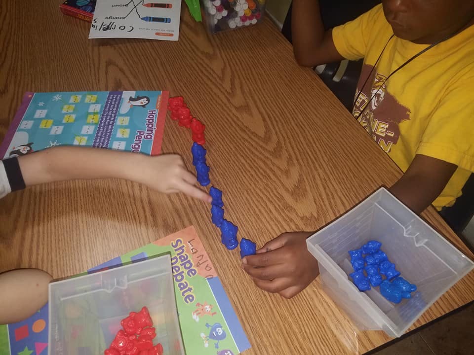 Two people playing with red and blue interlocking blocks on a wooden table