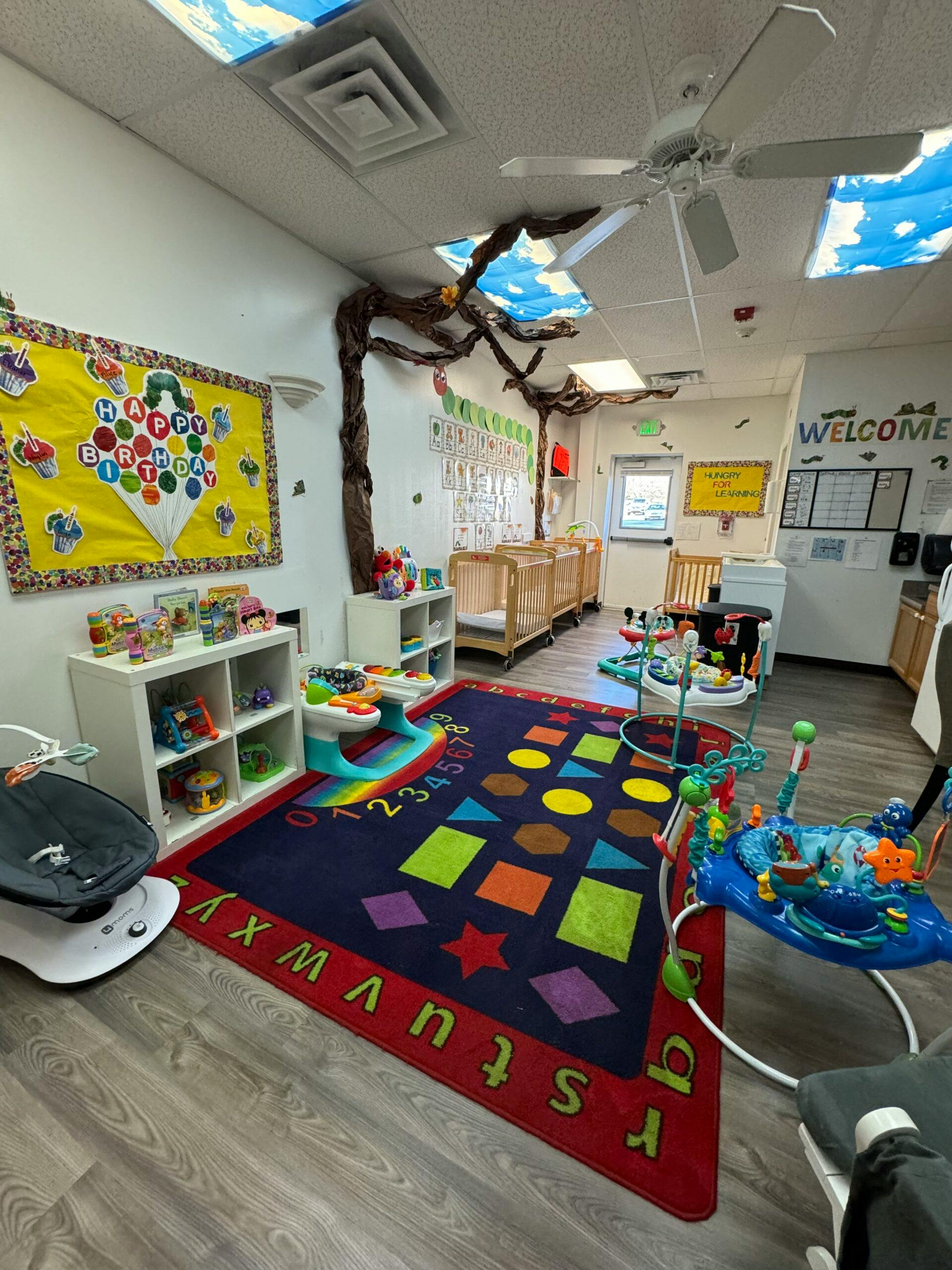 Infant and toddler classroom with cribs, playmat, and toys