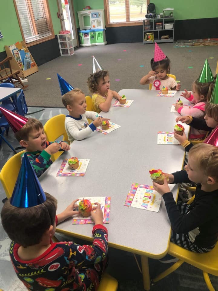 Children wearing party hats eating cupcakes at a table