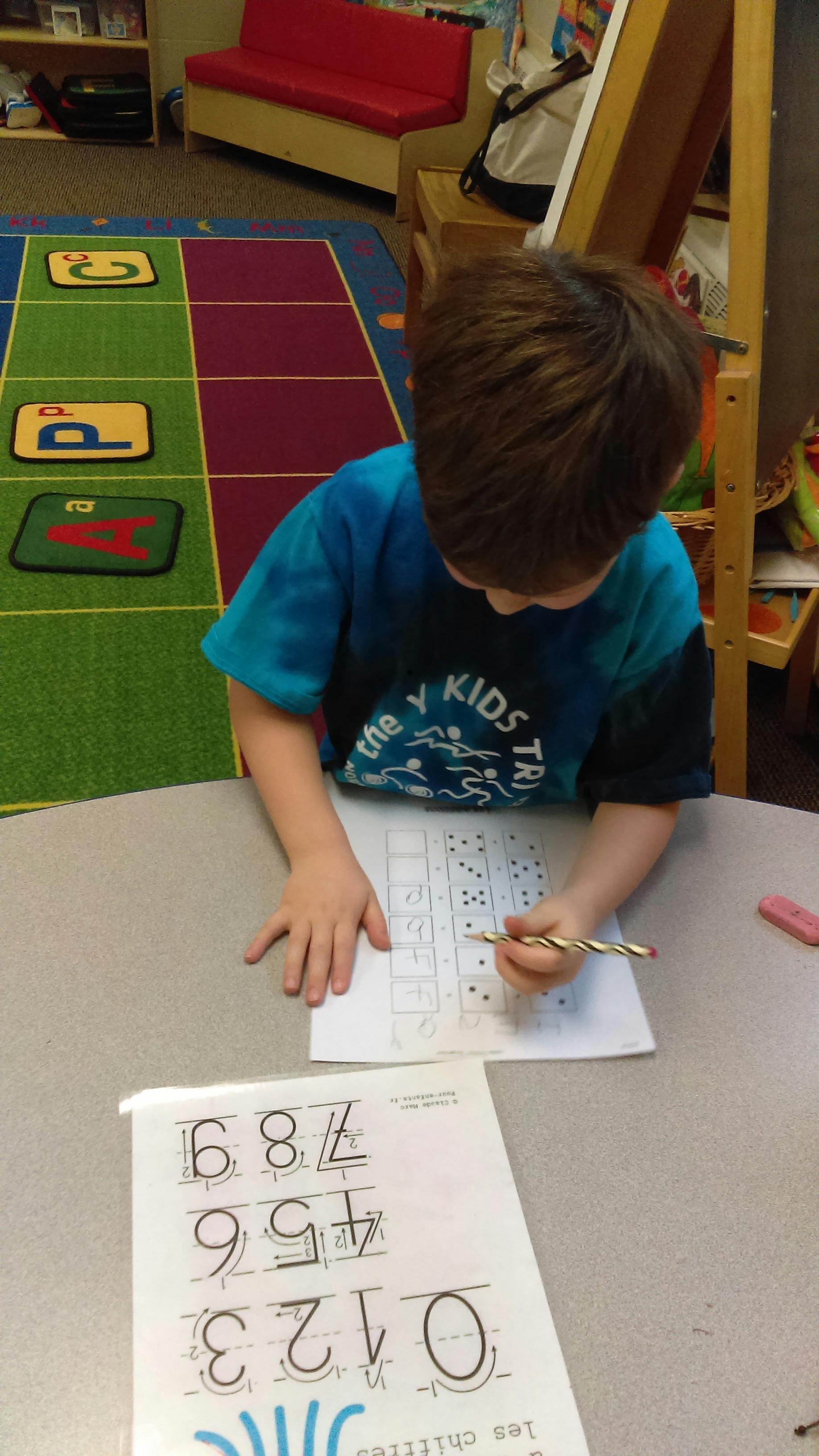 Child writing on a worksheet at a table in a classroom