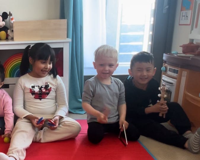 Three children sitting on a red mat indoors