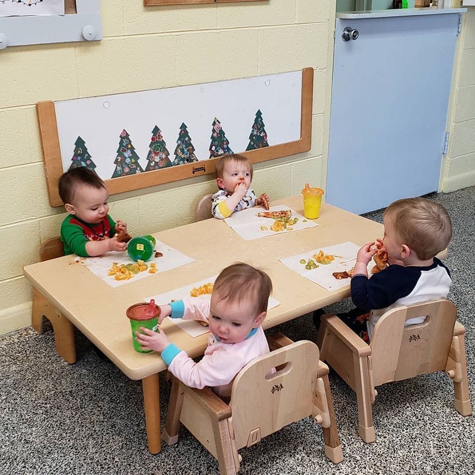 Four babies sitting at a small table in a classroom