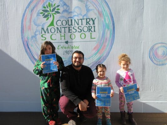 Adult and three children holding certificates in front of a school logo
