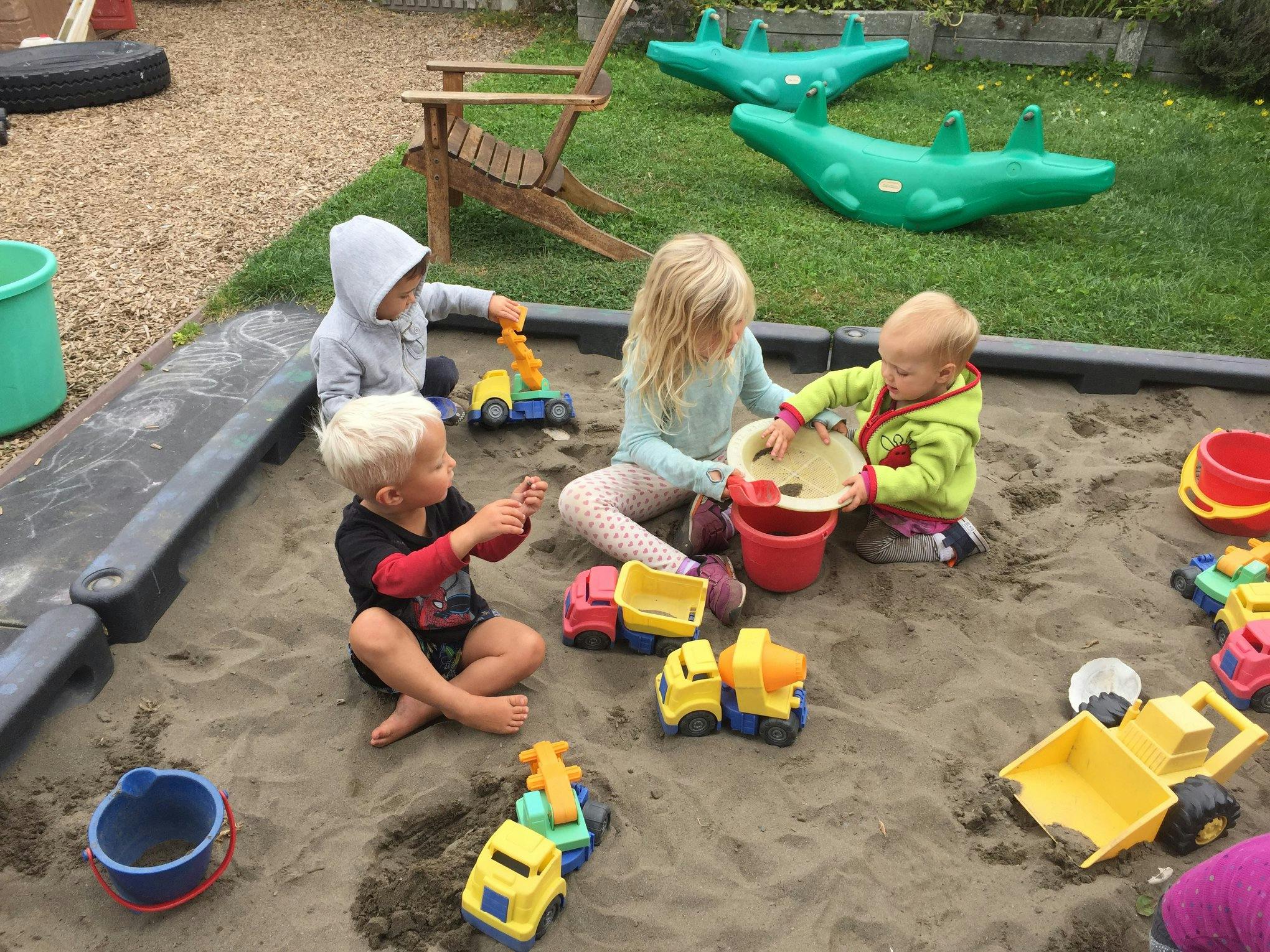 Children playing in a sandbox with toy trucks and buckets