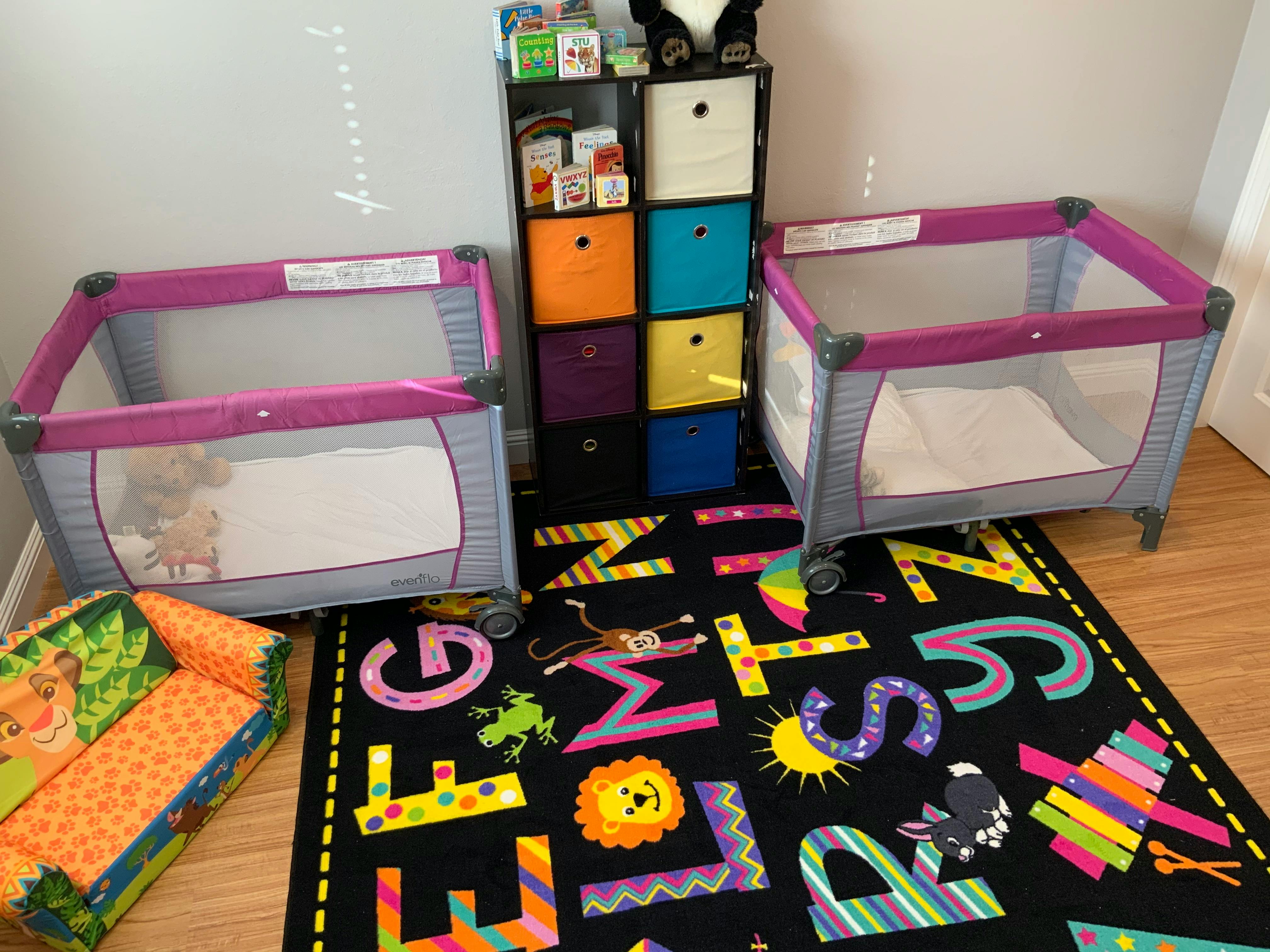 Two portable cribs and a colorful alphabet rug in a room