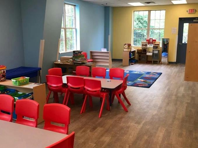 Classroom with small red chairs and tables, blue rug, and various play items