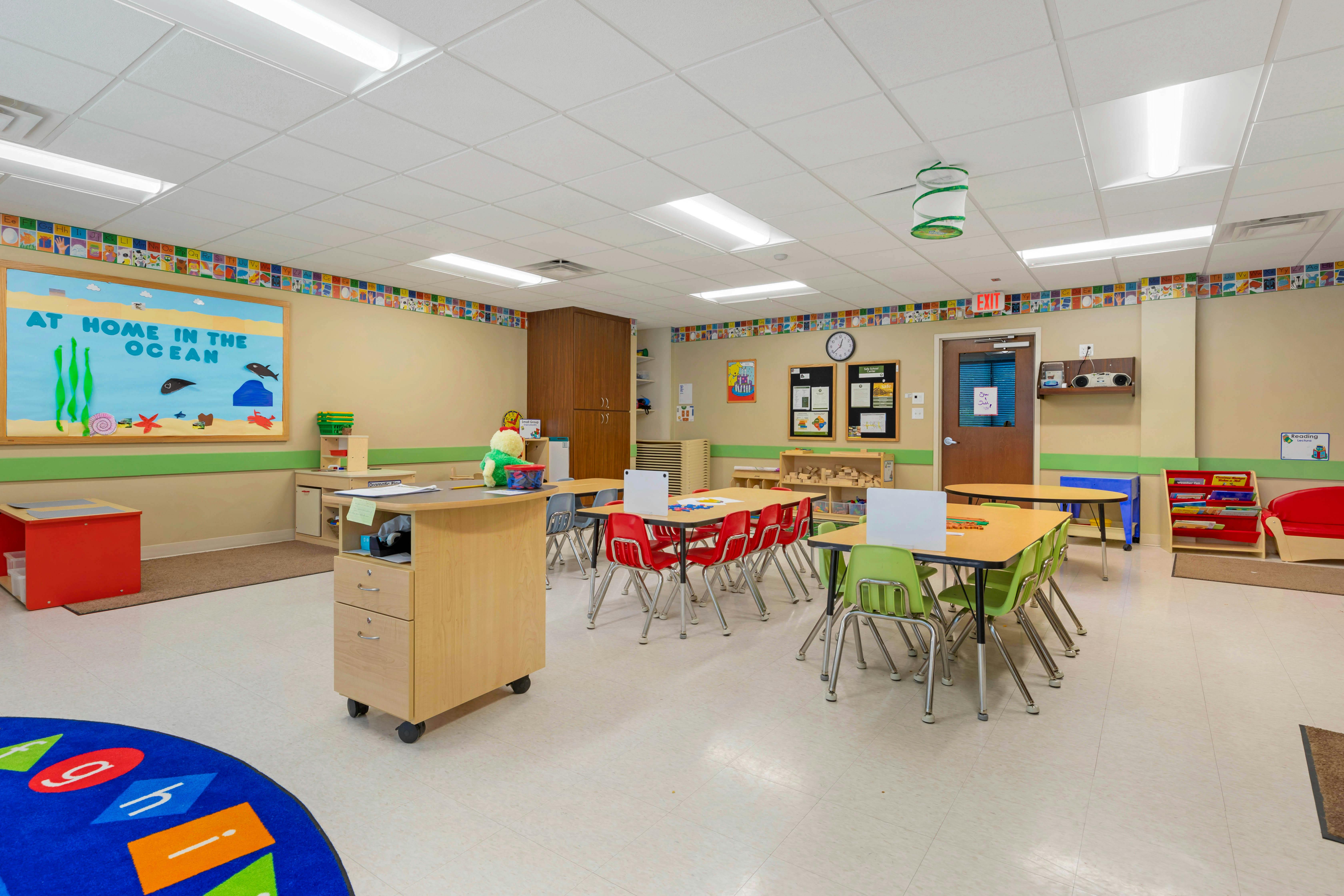 An empty classroom with small tables and chairs for children