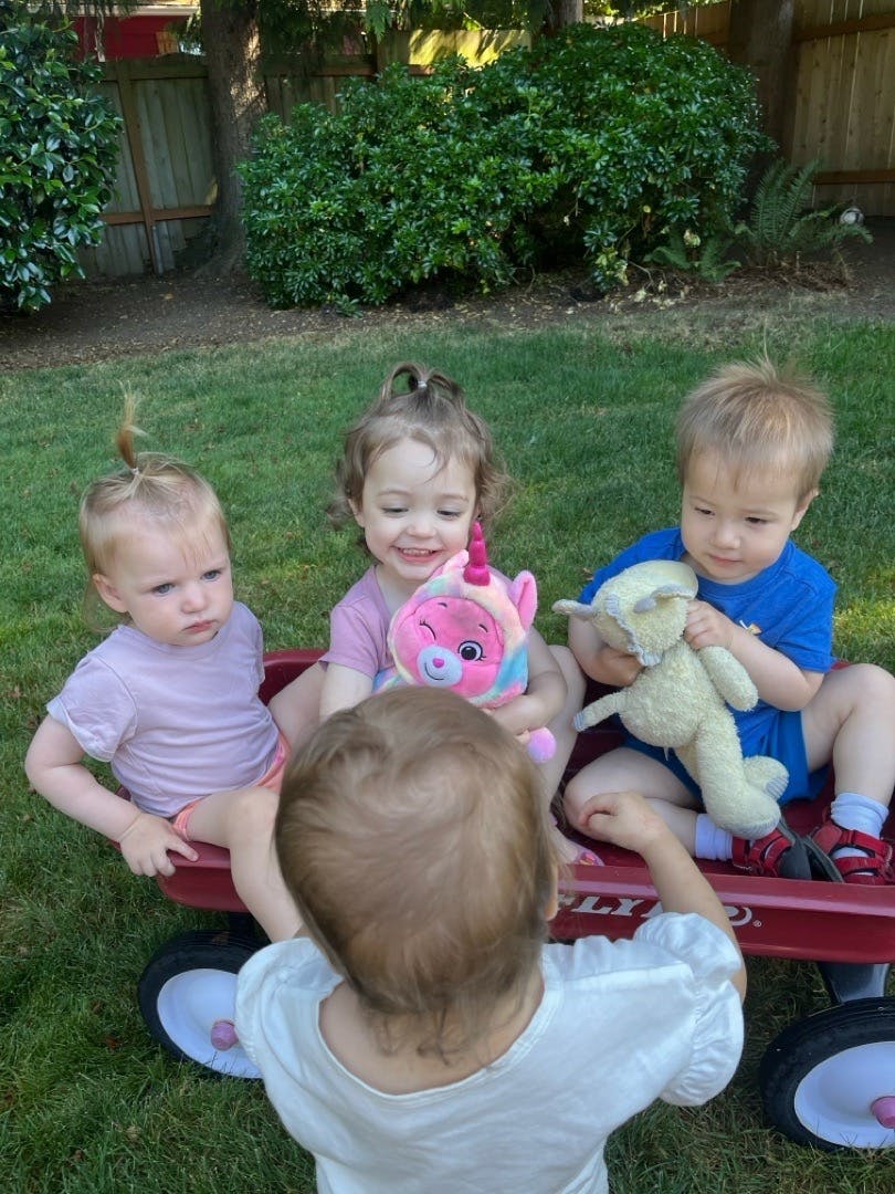 Three children sitting in a wagon with stuffed animals, one child standing in front