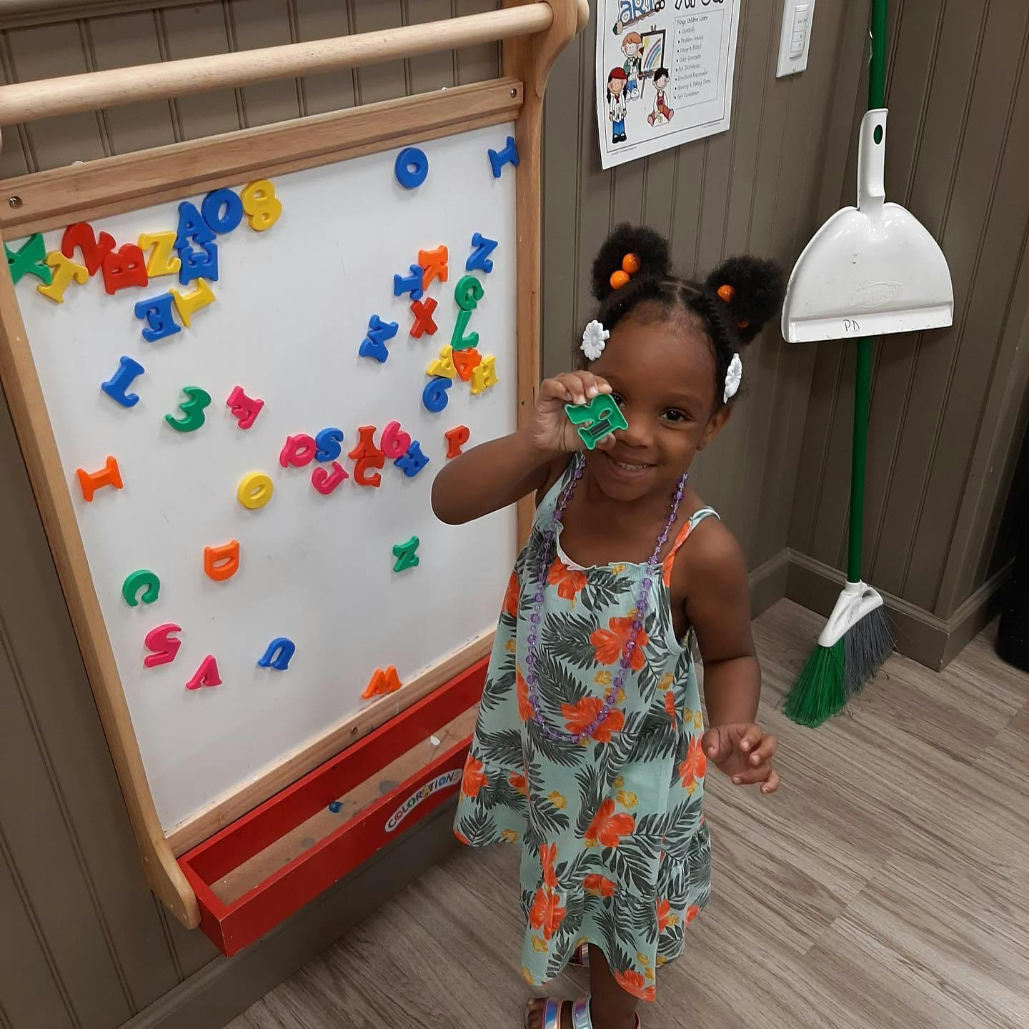 Child holding a green magnetic letter in front of a whiteboard with letters