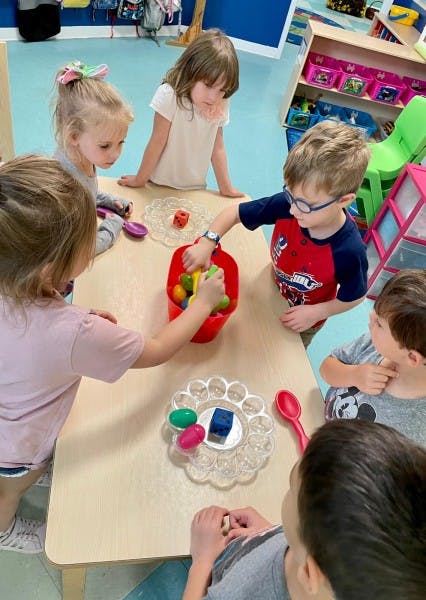 Children at a table playing with plastic eggs and a red bucket