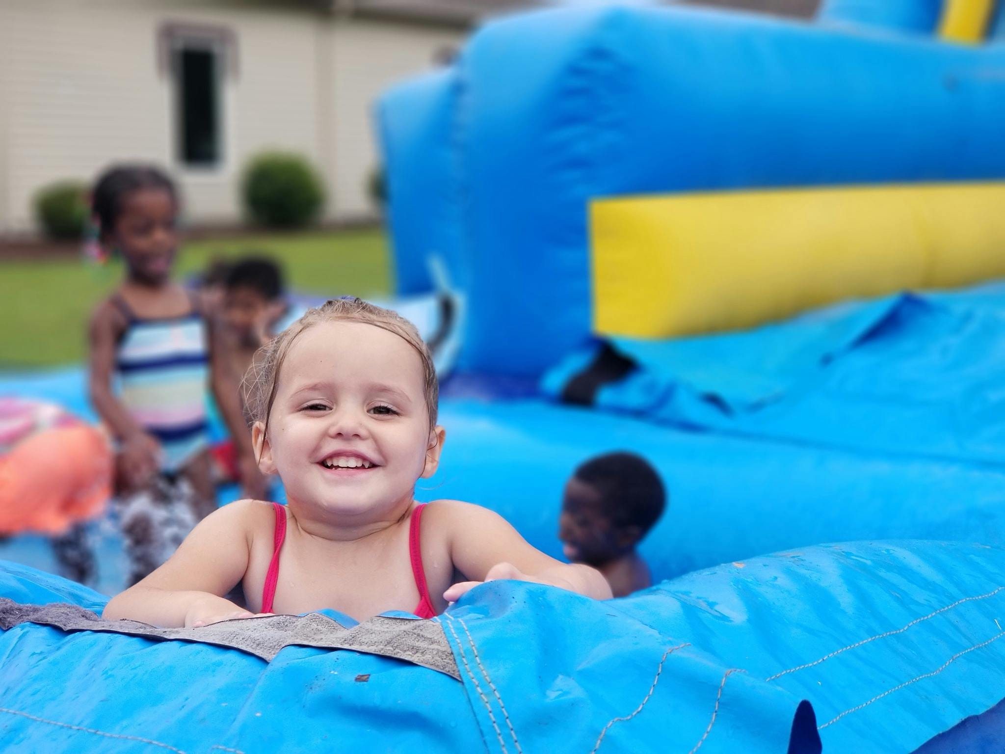 Child in a red swimsuit on a blue inflatable slide with other children