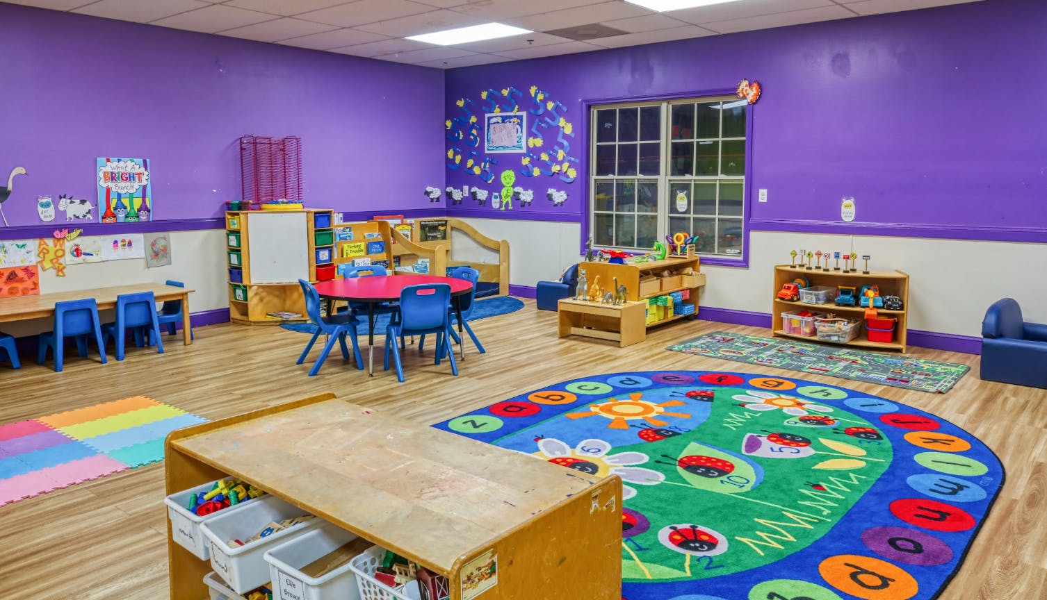 Colorful classroom with small tables and chairs, a play rug, and toys