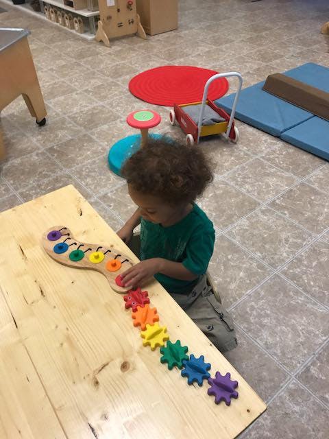 Child playing with a colorful gear toy on a wooden table