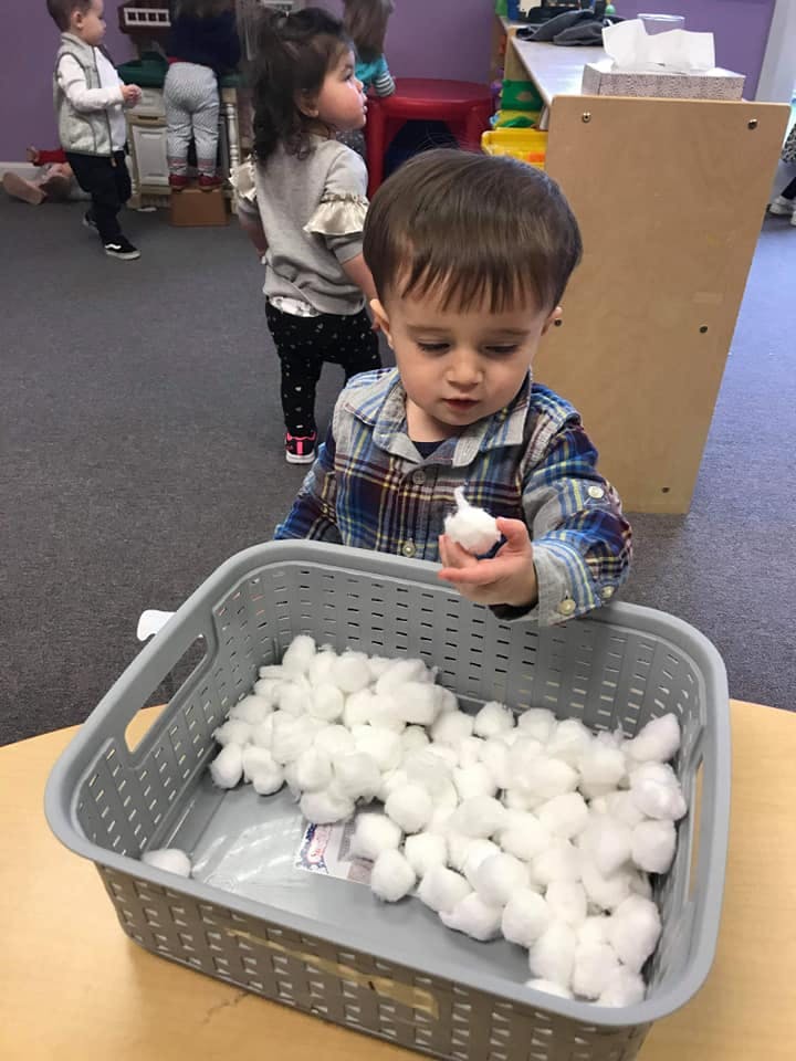 Child holding a cotton ball over a basket of cotton balls