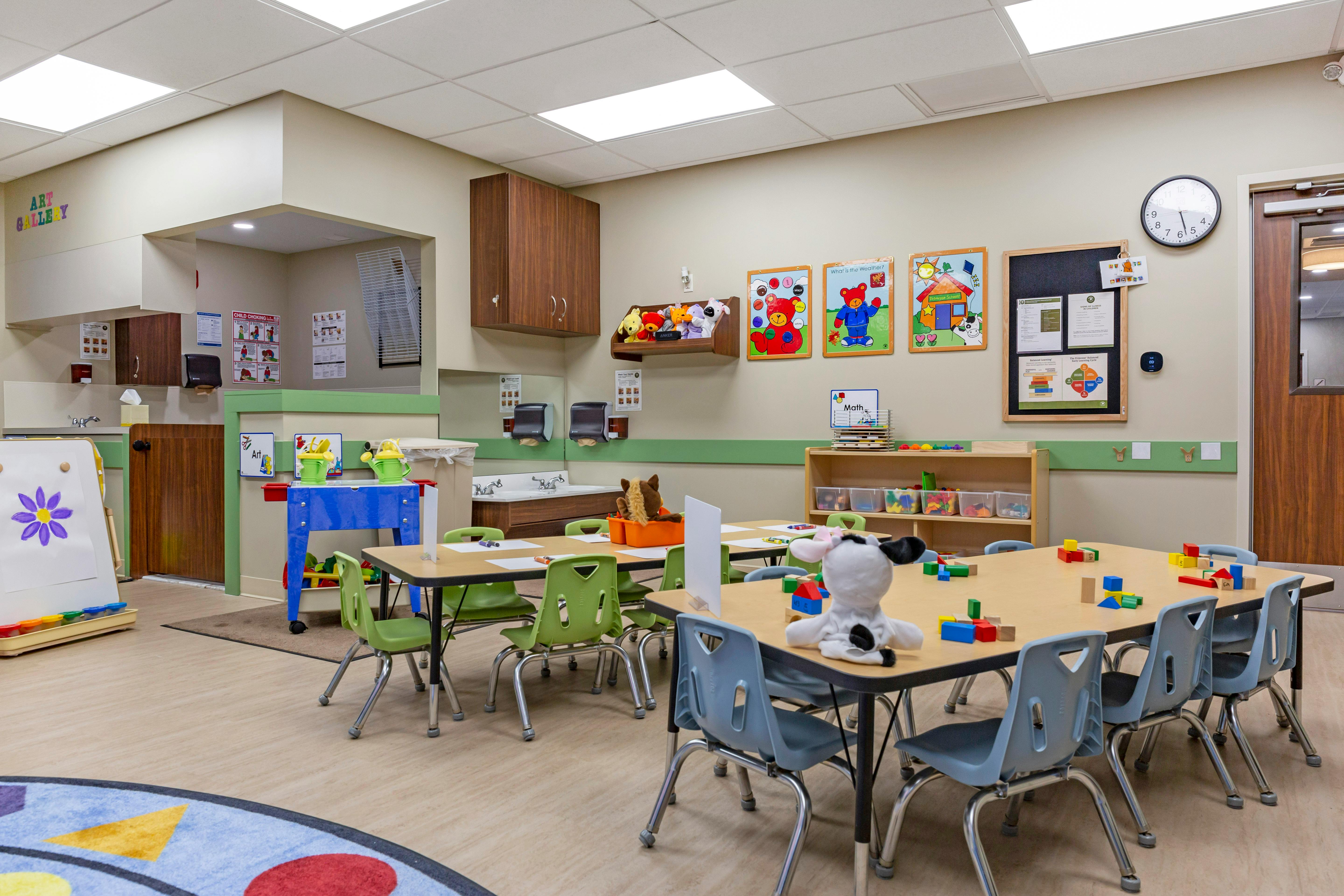A colorful classroom with small tables and chairs, toys, and educational posters