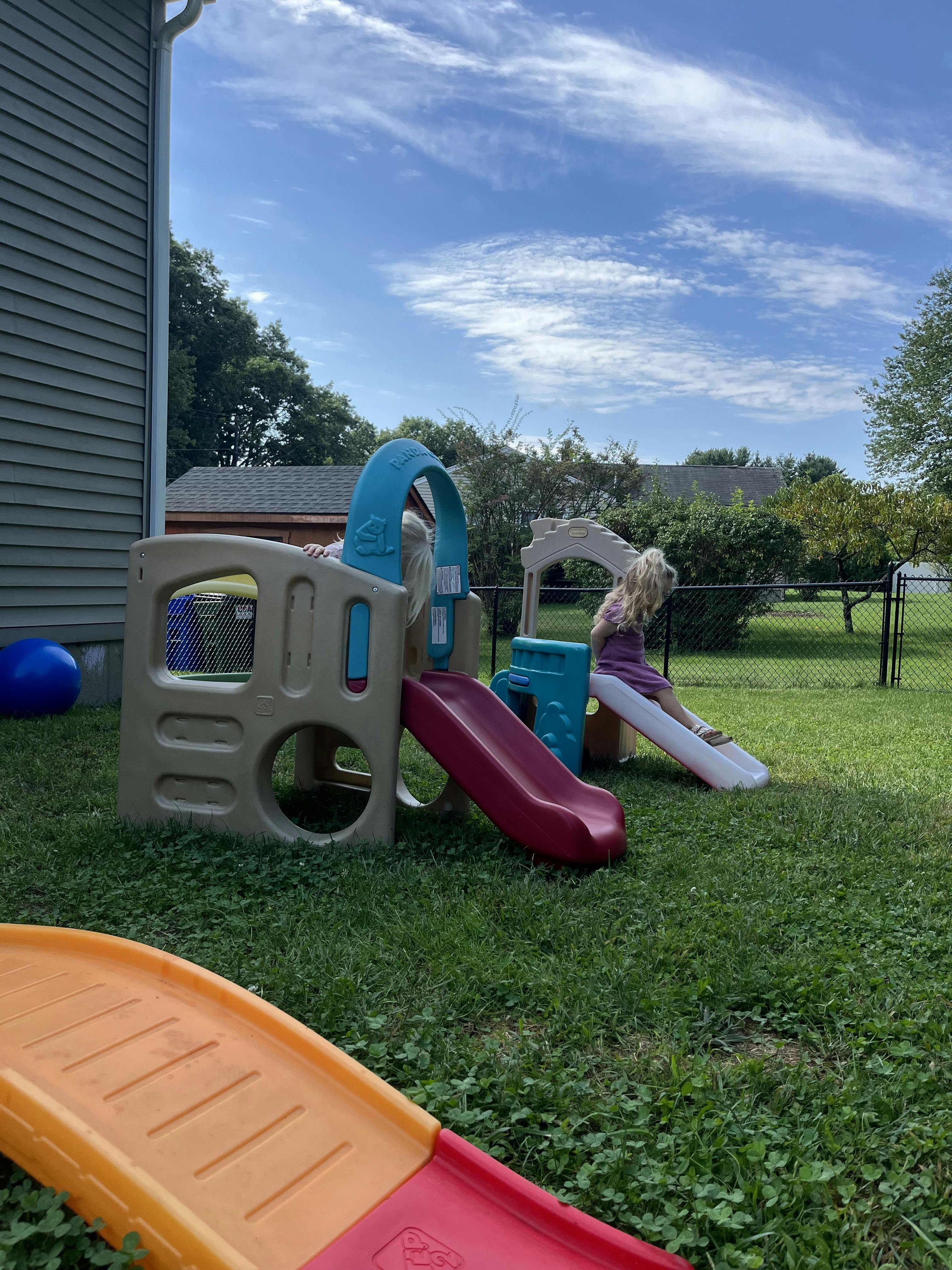 Children playing on a plastic jungle gym in a backyard