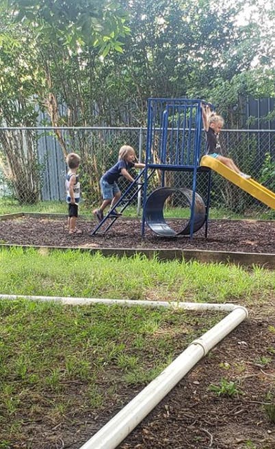 Three children playing on a playground structure with a slide and climbing structure