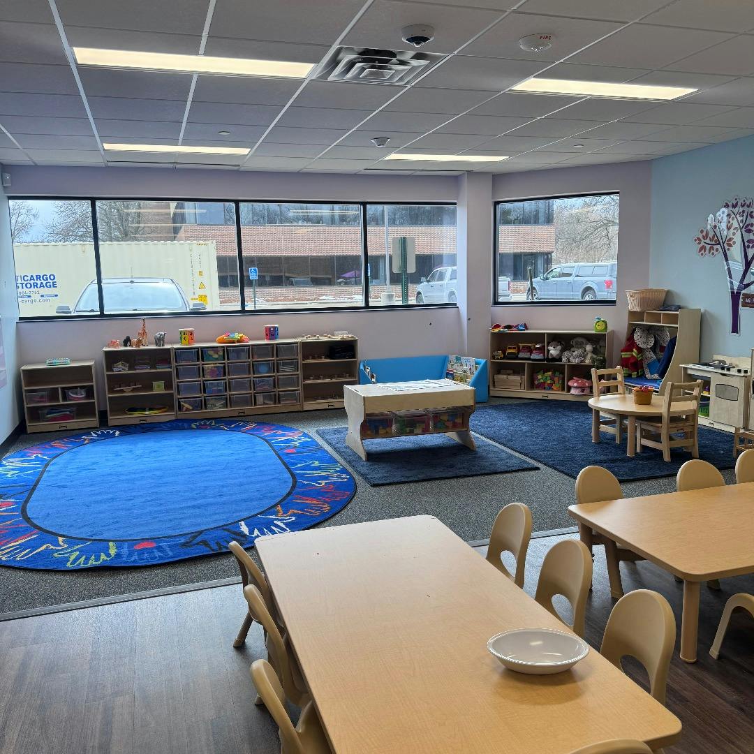 Children's classroom with small tables, chairs, rugs, and storage shelves