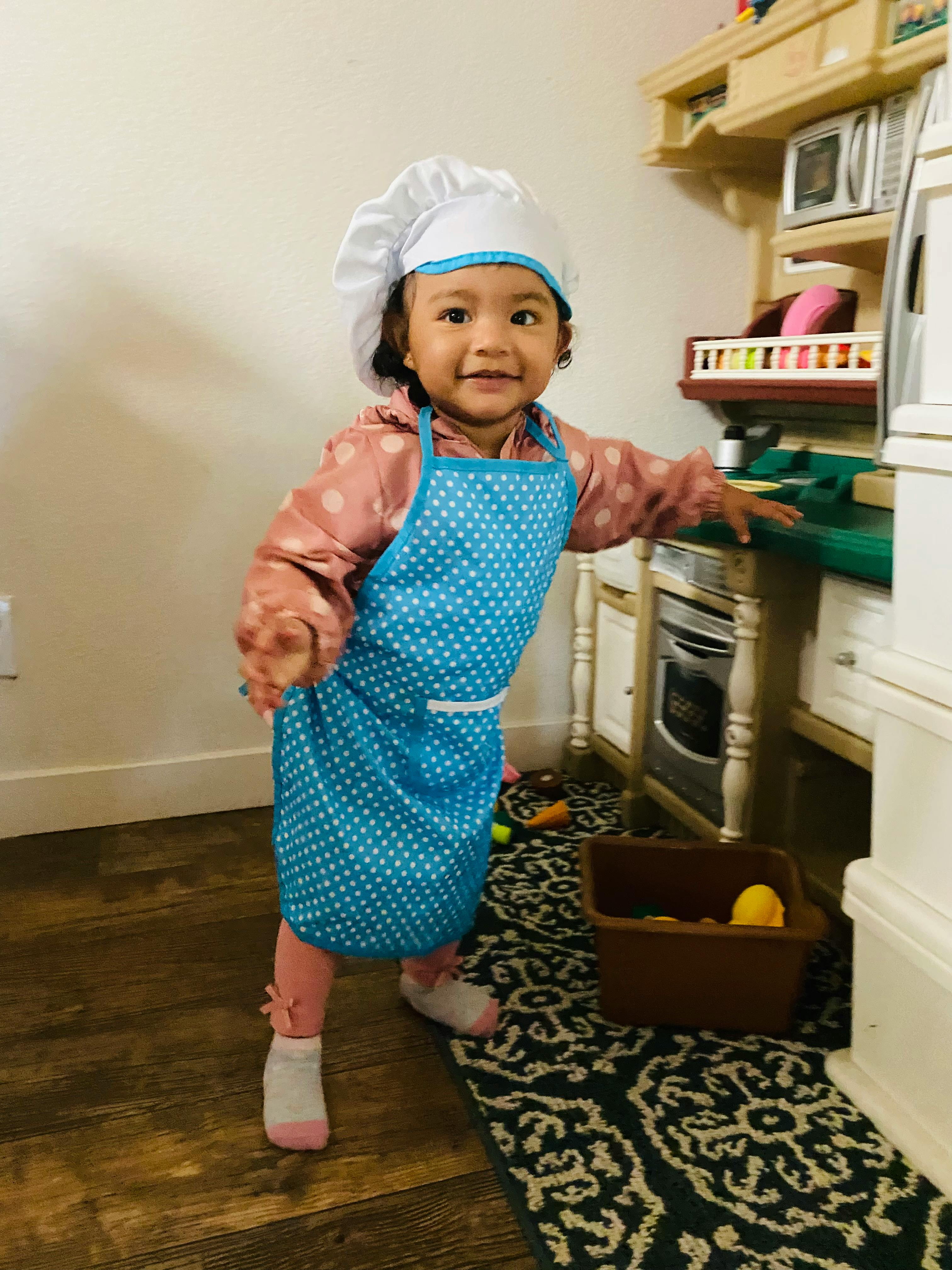 Child wearing a chef hat and apron in a play kitchen