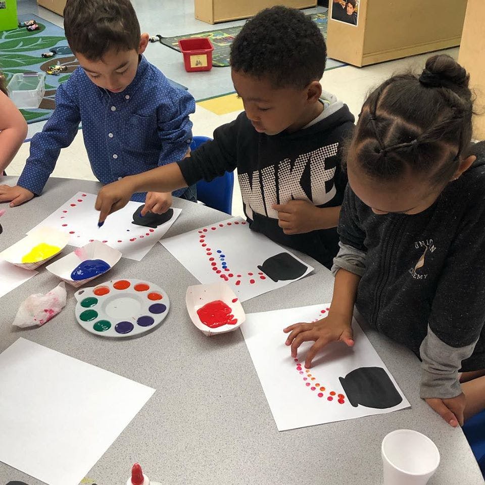 Three children painting with sponges and dots of paint on paper