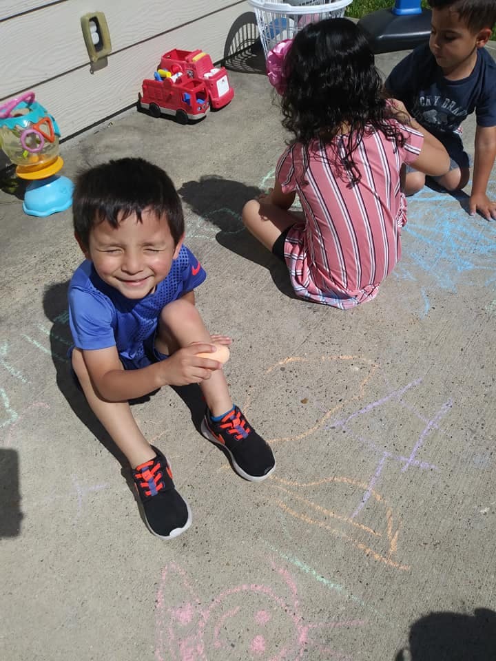 Child sitting on ground with eyes closed, other children in background