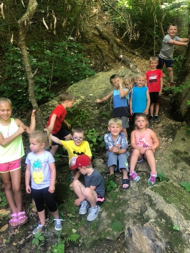 Group of children playing outdoors on a rocky, wooded incline
