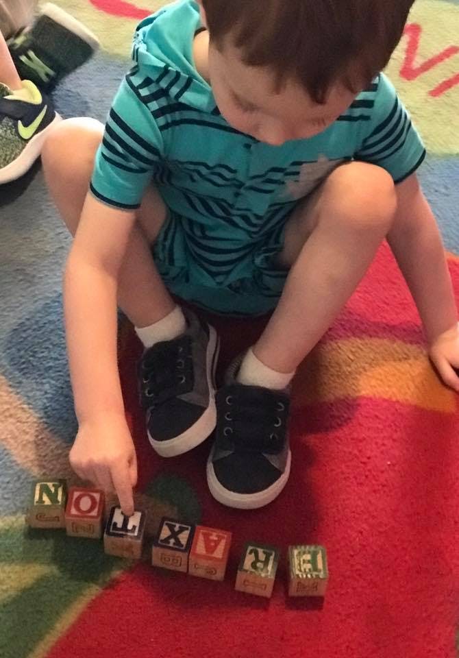 Child sitting on a rug, pointing at letter blocks