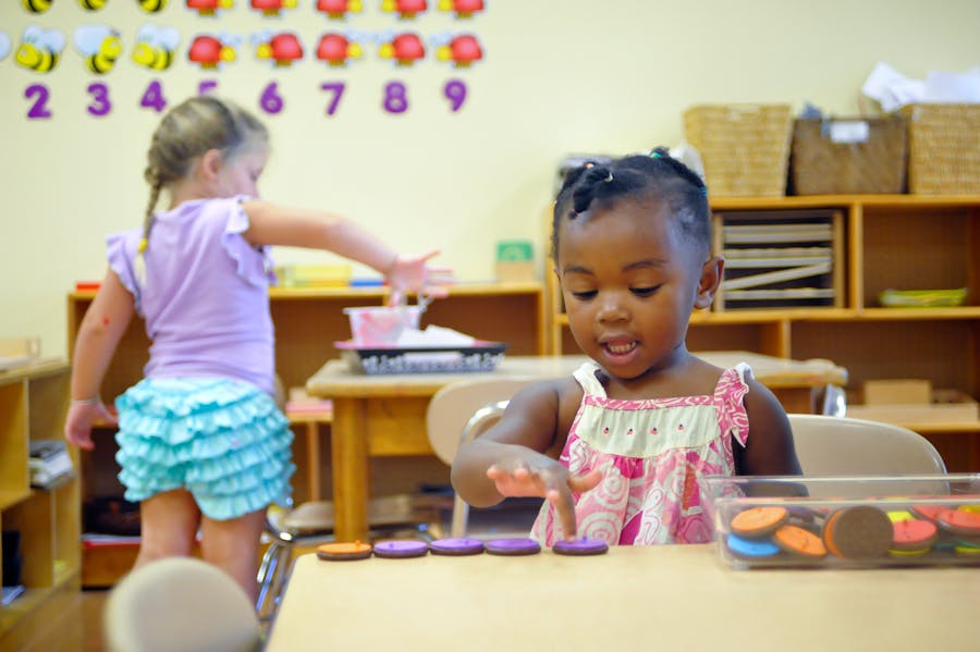 Child playing with colorful discs at a table in a classroom
