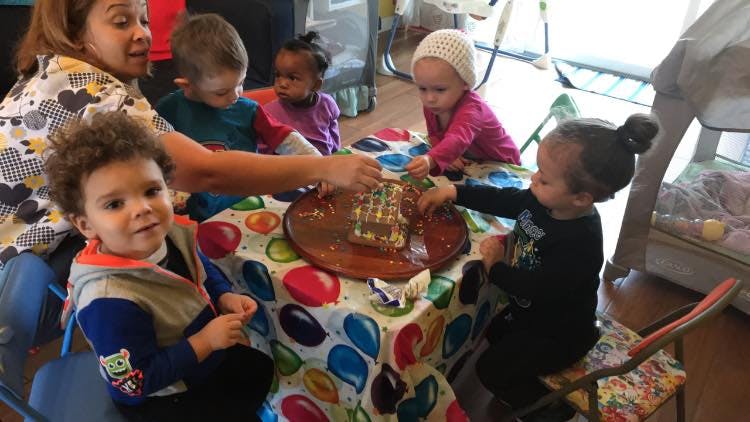 Adult and children decorating a gingerbread house at a table