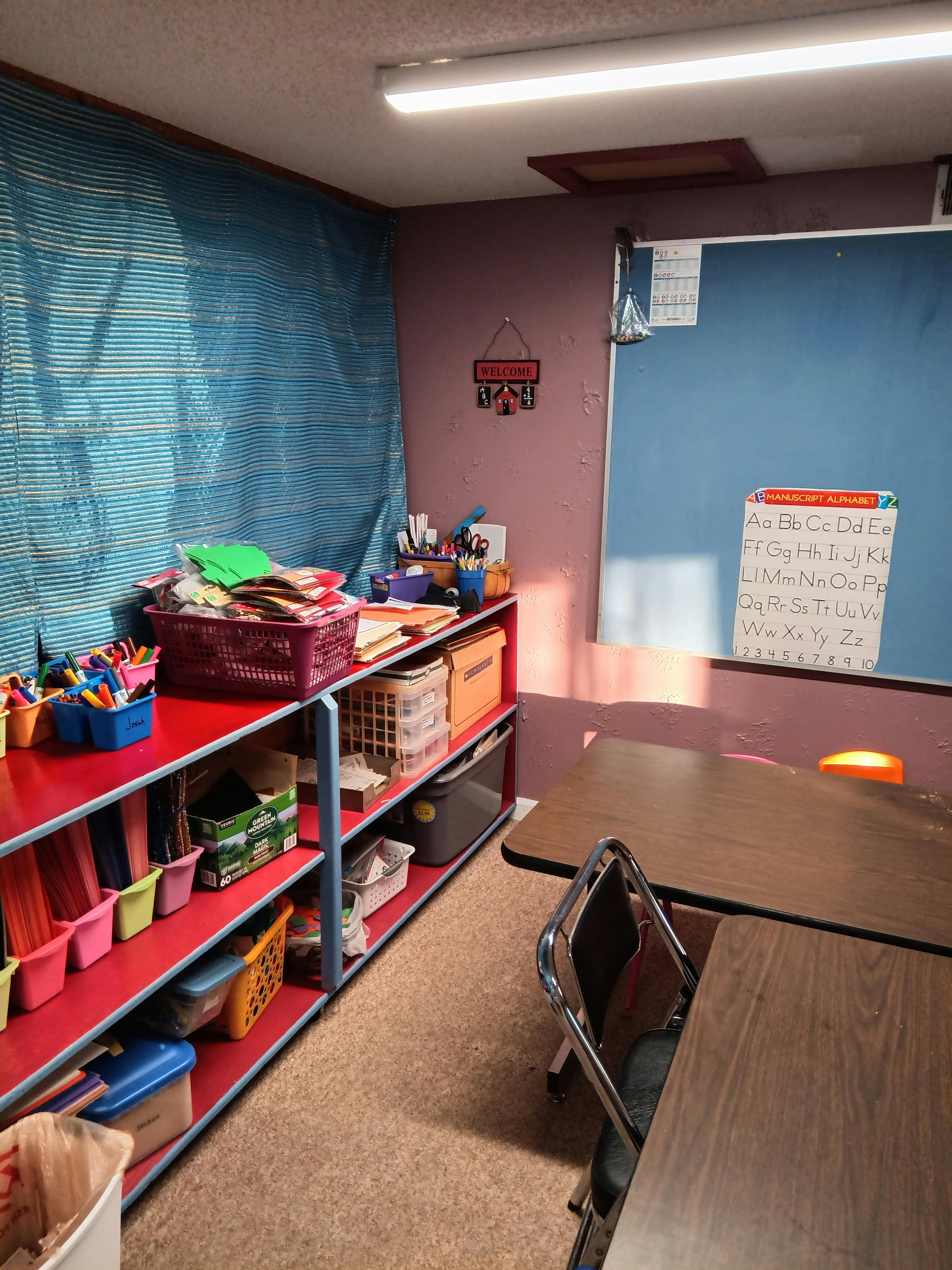 Classroom with shelves of supplies, a chalkboard, and student desks
