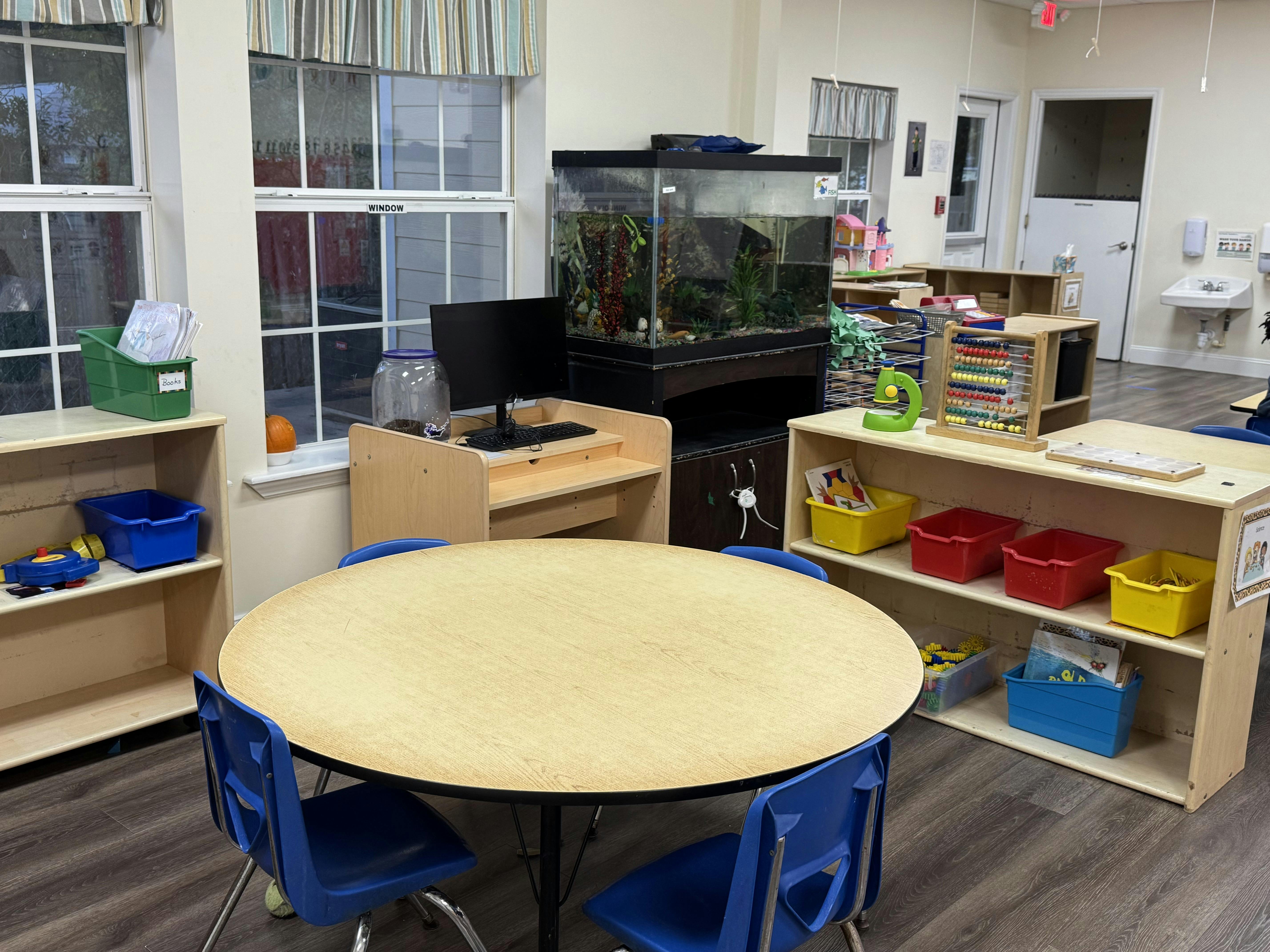 Classroom with round table and chairs, shelves, and a fish tank