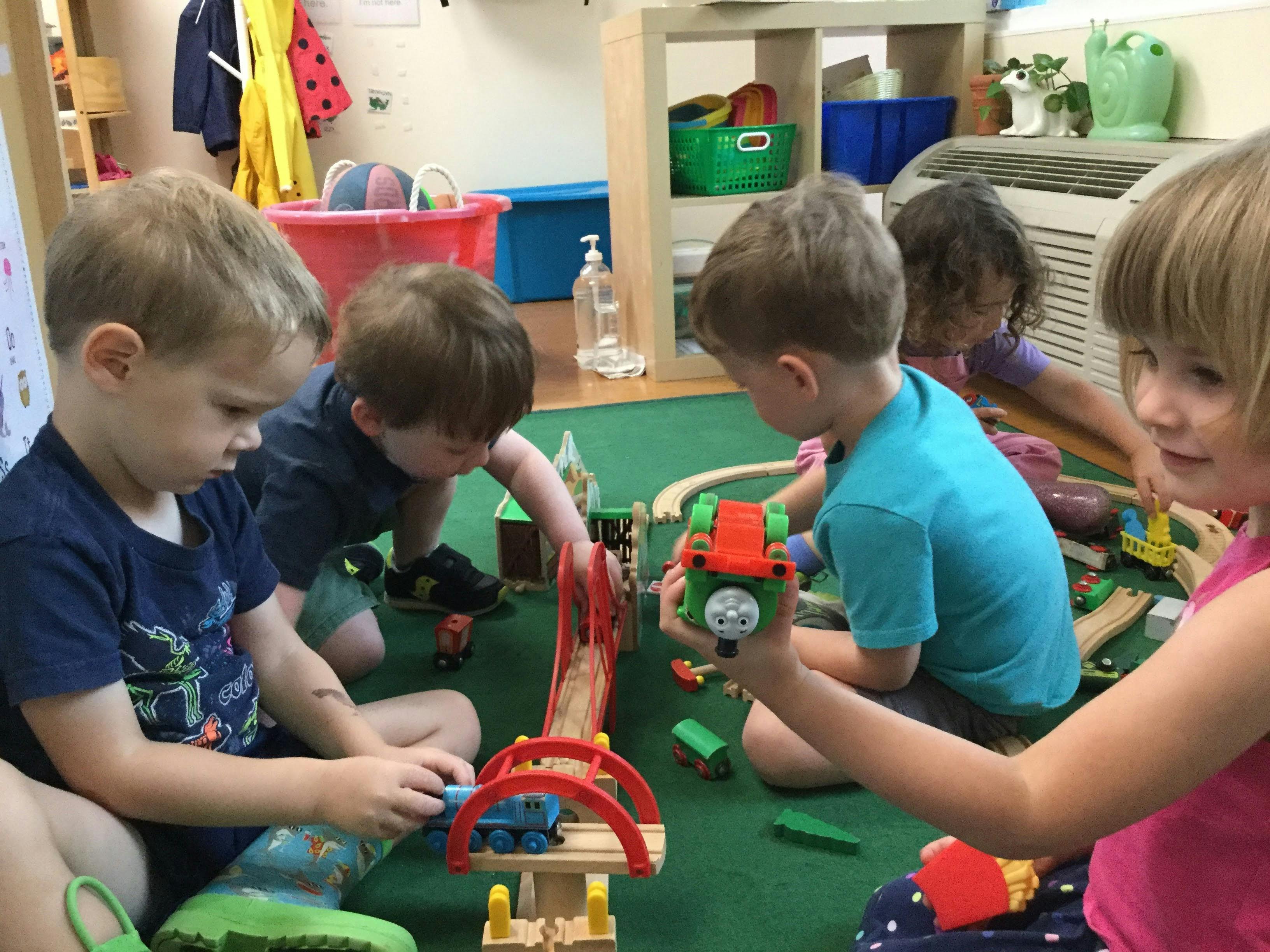 Four children playing with toy trains on a green mat