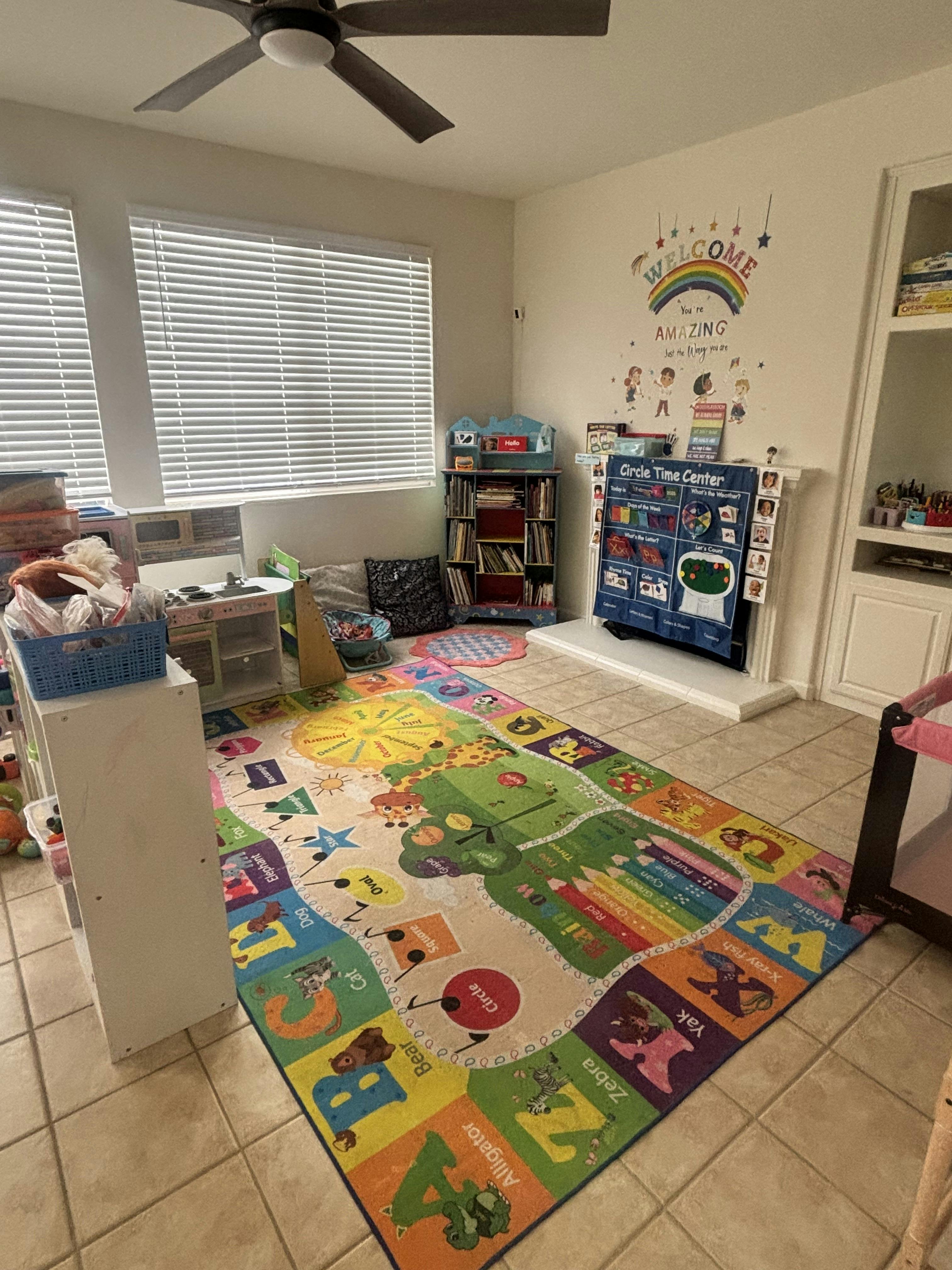 Children's play area with a colorful alphabet rug, toy kitchen, and bookshelves
