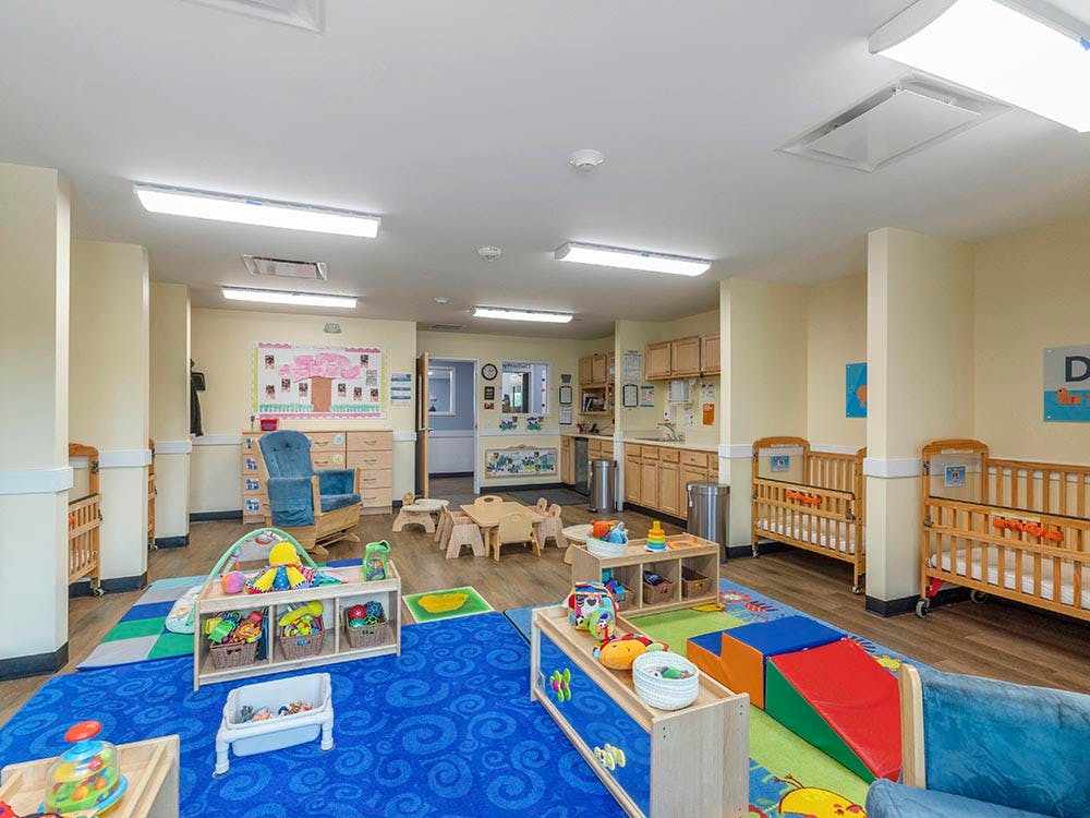A childcare classroom with cribs, play mats, and small tables