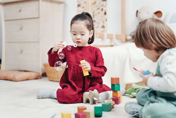 Child blowing bubbles while another child plays with blocks