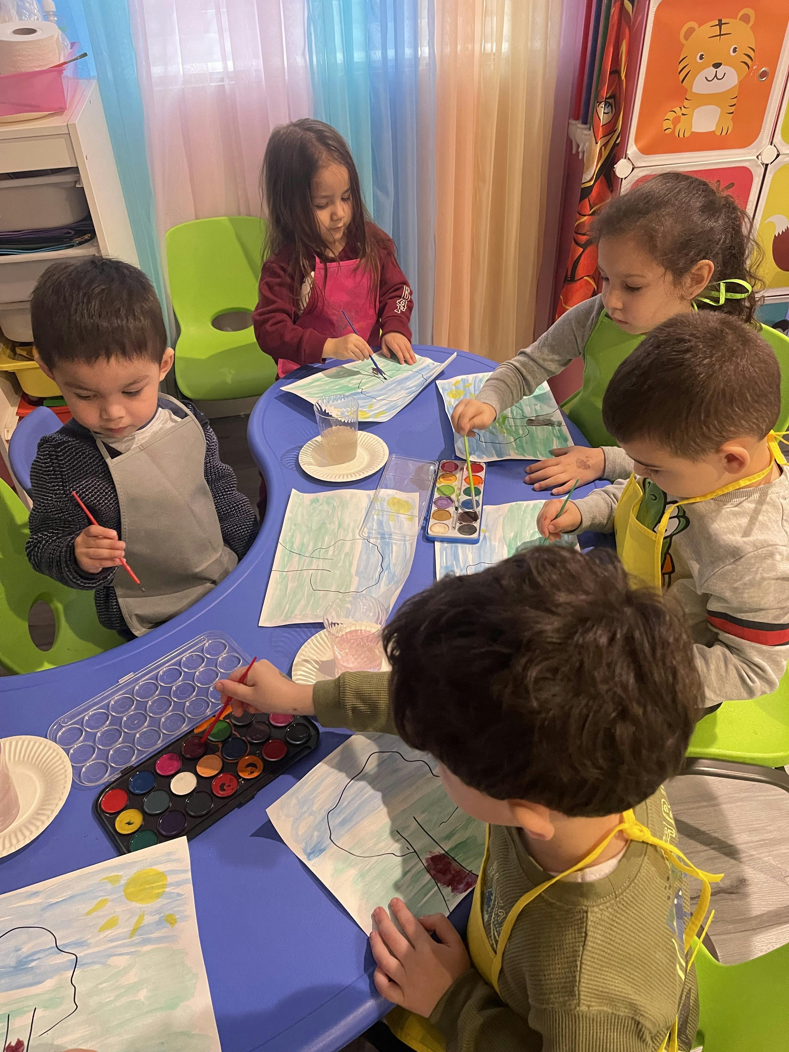 Four children painting at a blue table in a classroom