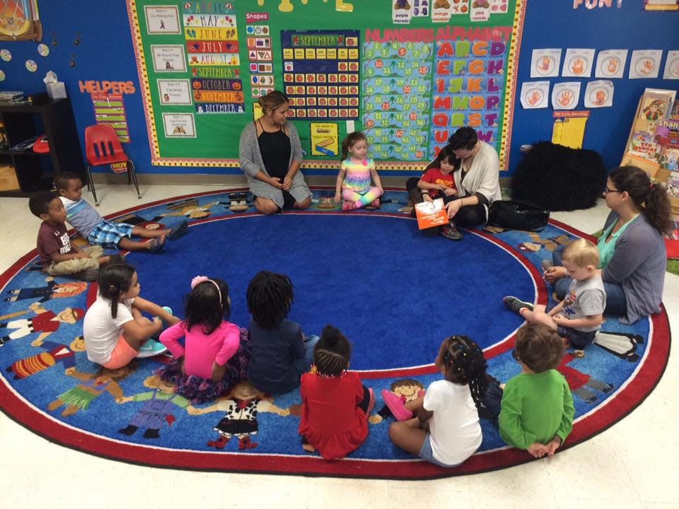 Adults and children sitting on a rug in a classroom